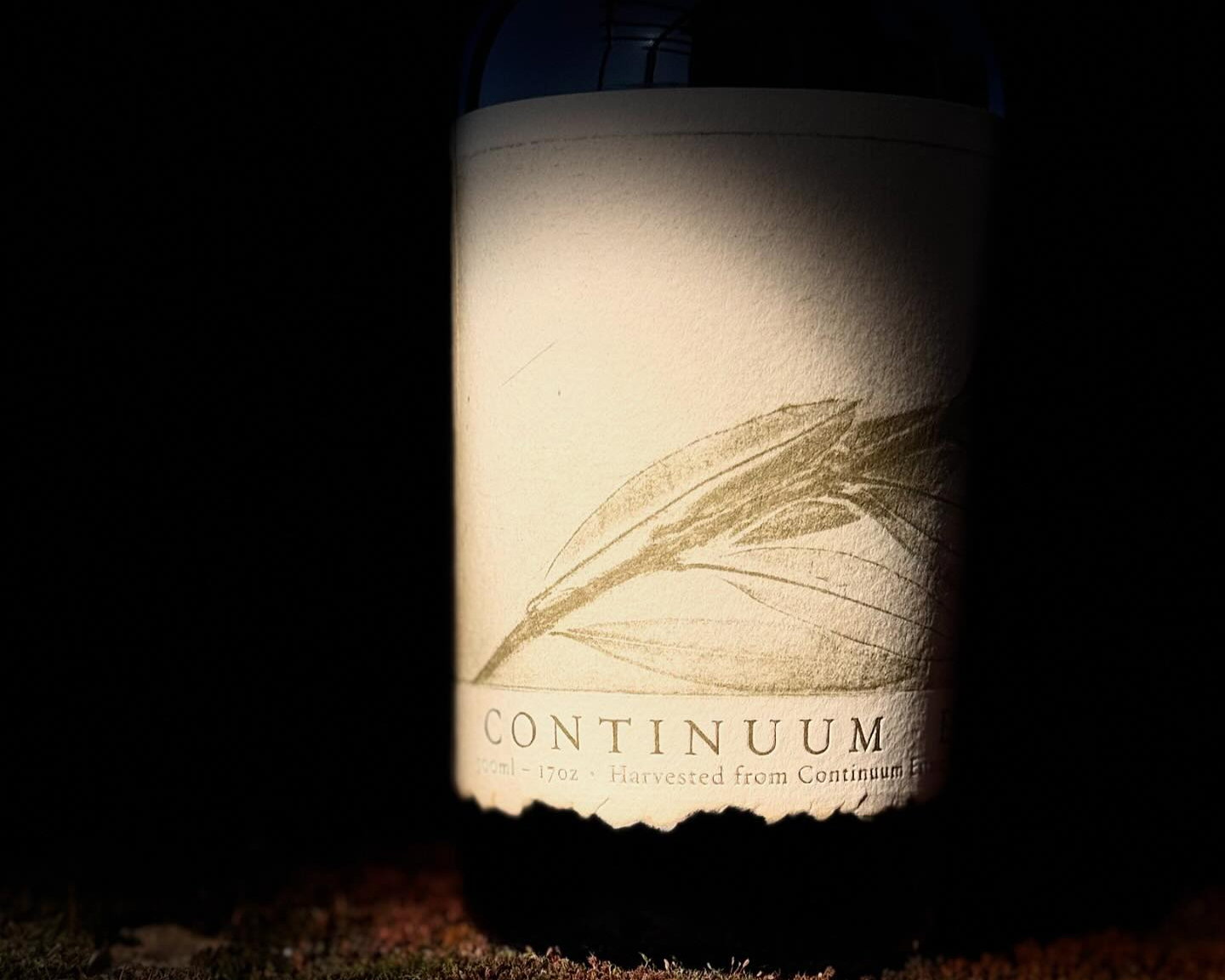 Wine bottle with label showing "CONTINUUM" in shadowed lighting, featuring a leaf design. The background is dark, creating a moody atmosphere.