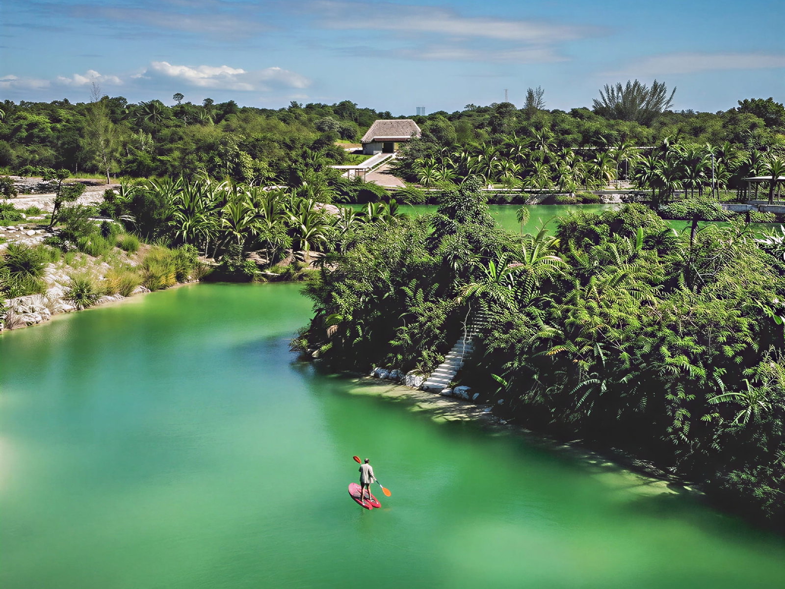 Person paddleboarding at Wakax Hacienda on a turquoise river through lush green jungle. Bright sunny day, clear blue sky. Peaceful and serene setting.