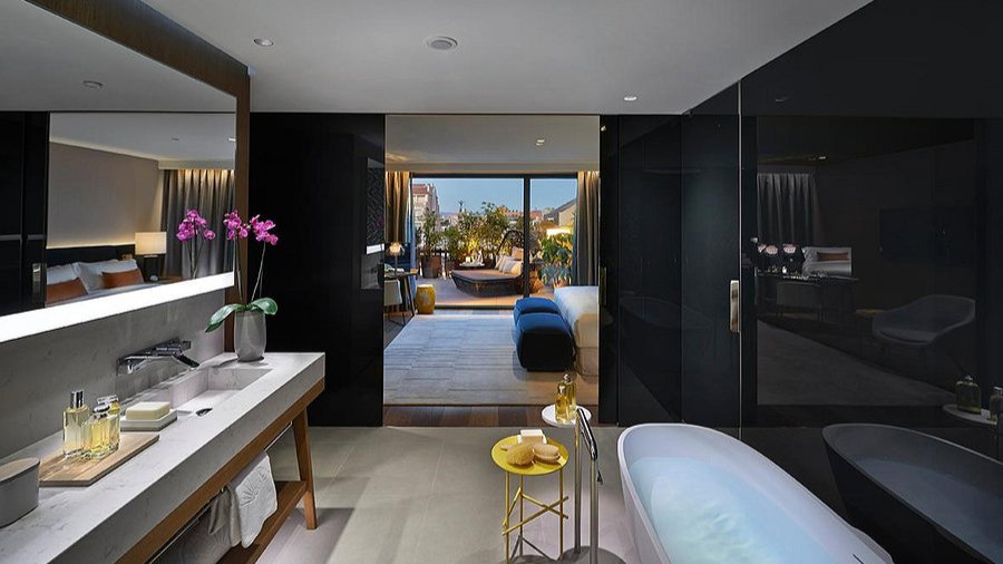 Luxurious modern bathroom with a freestanding tub, orchid on sink, and large mirror. Opens to a cozy terrace with outdoor seating.