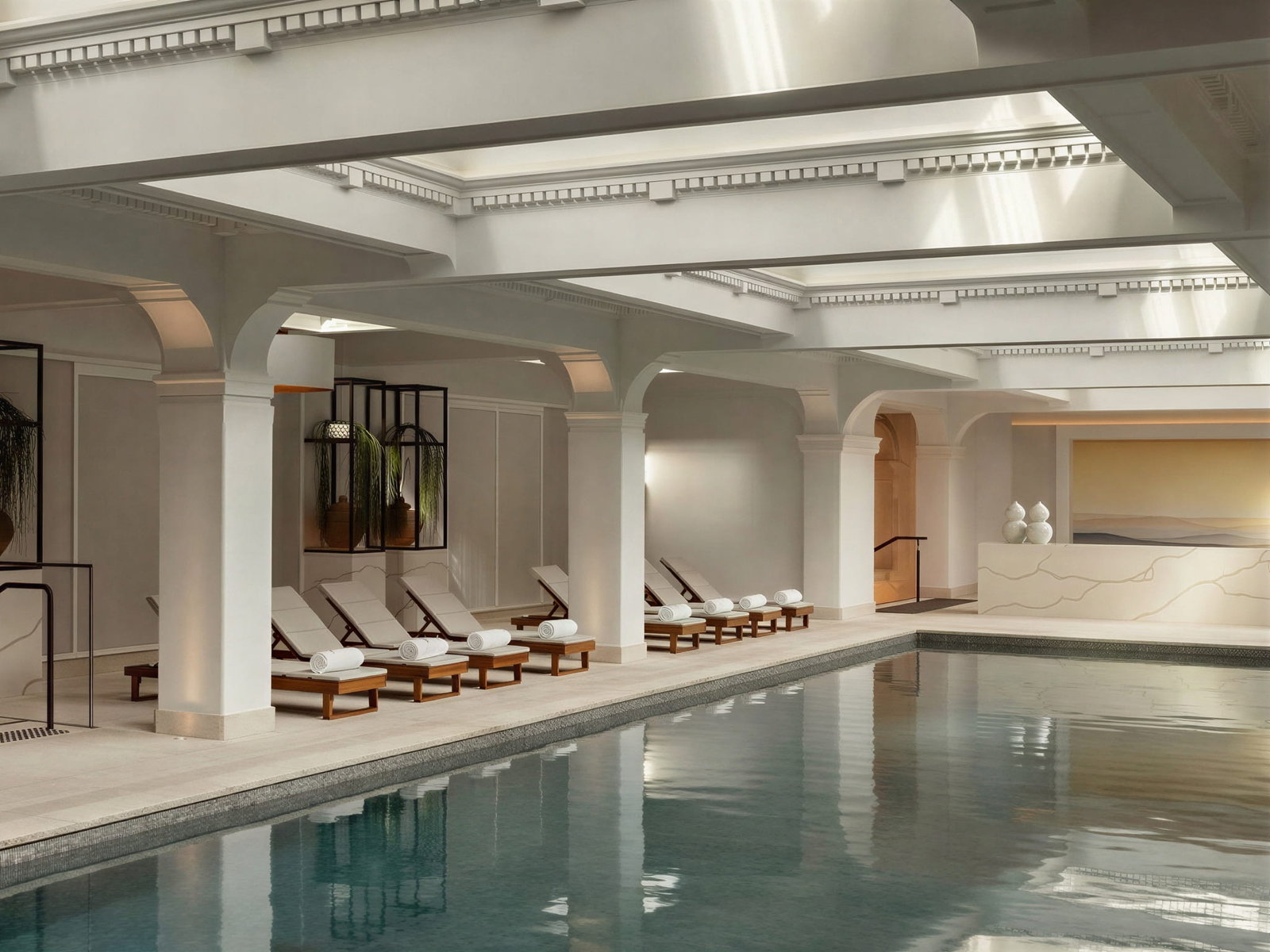 Indoor swimming pool at Capella Sydney with beige loungers lined up, elegant white columns, serene atmosphere. Soft lighting highlights architectural details.