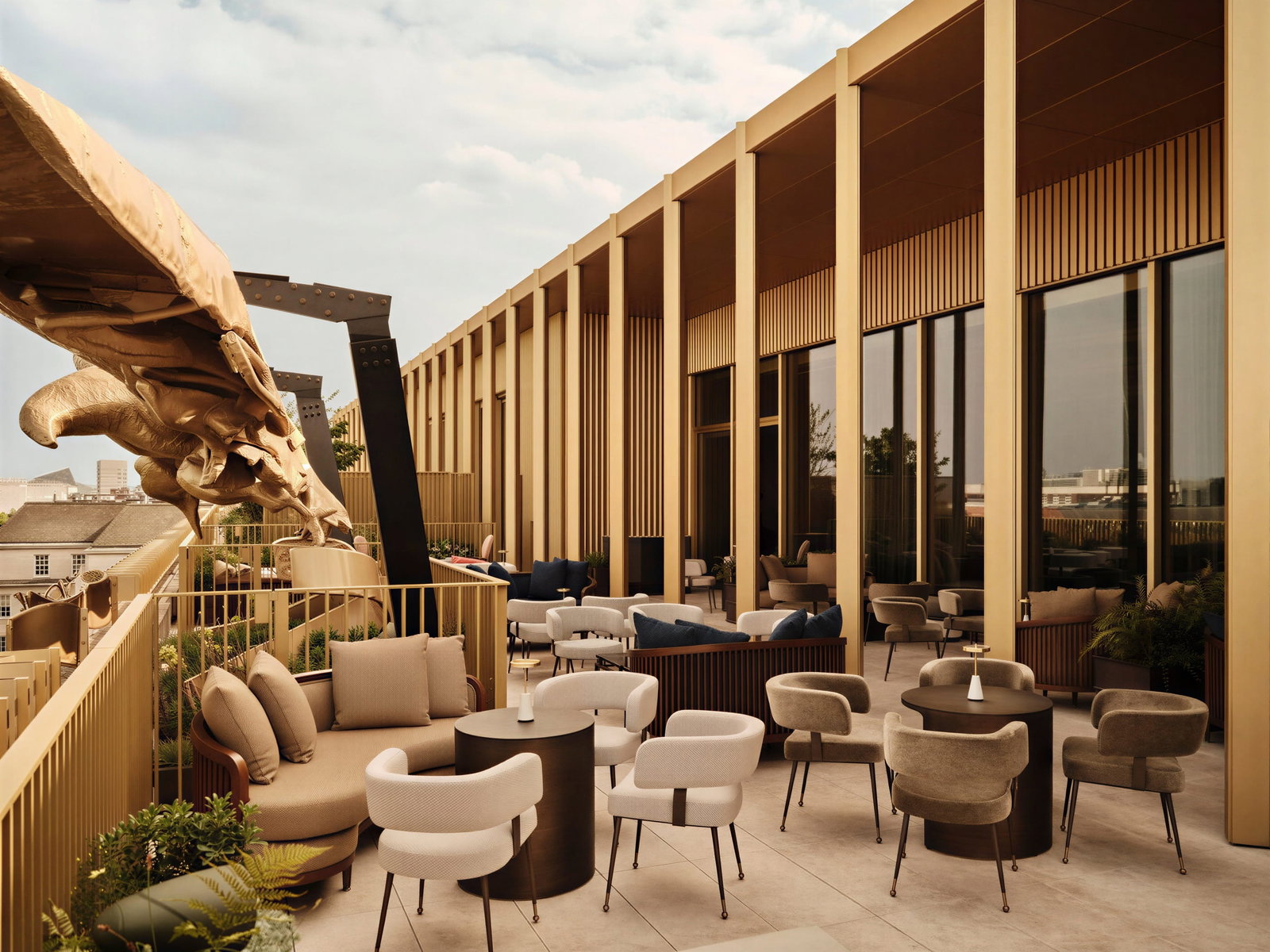Elegant Eagle Bar rooftop terrace at The Chancery Rosewood with beige and gray seating, gold accents, and a large sculpture. Modern design, urban backdrop, calm ambiance.