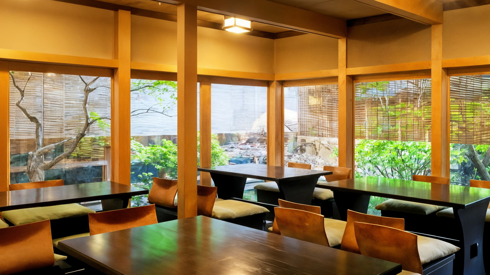 Wooden tables and chairs in a bright, serene Japanese-style room. Large windows reveal a garden with trees and lush greenery outside.
