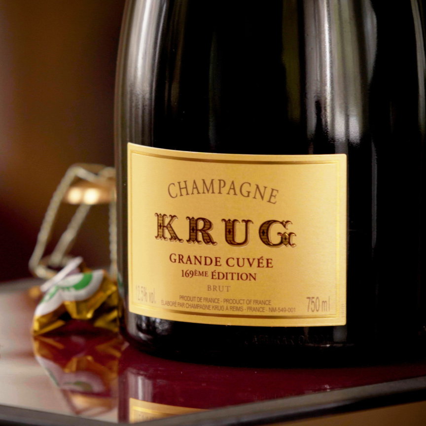 Bottle of Krug Grande Cuvée champagne on a reflective surface with wrapped candies nearby. Label text includes "Champagne Krug Grand Cuvée."