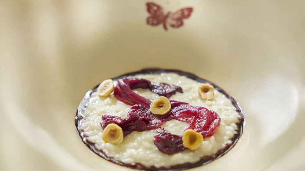 Risotto garnished with red beets and nuts in a cream-colored bowl with a butterfly design. The setting is elegant and inviting.