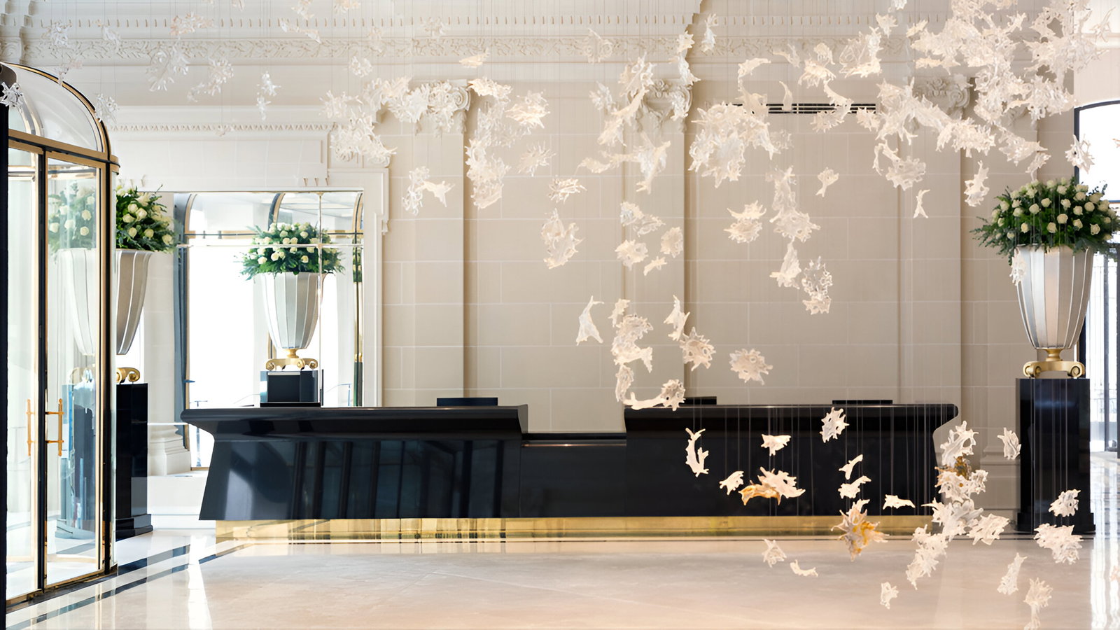 Elegant hotel lobby with white floral patterns suspended mid-air. Black modern desk and large vases with white flowers in the background.