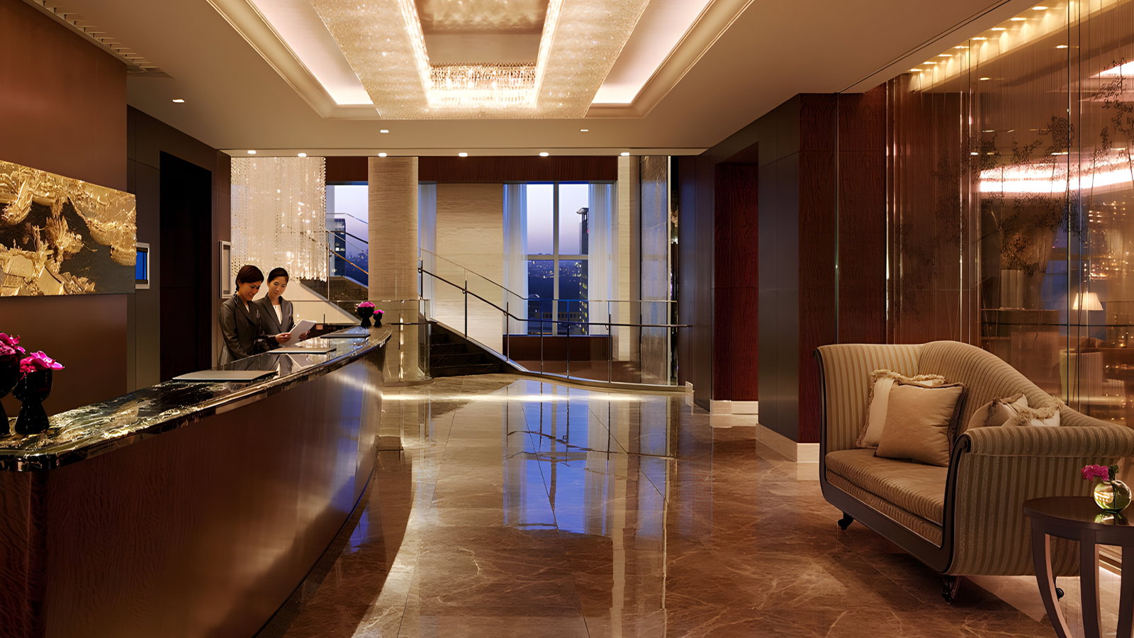 Elegant hotel lobby with two staff at a reception desk, large chandelier, marble floor, and a cozy couch. Flowers and a city view add warmth.