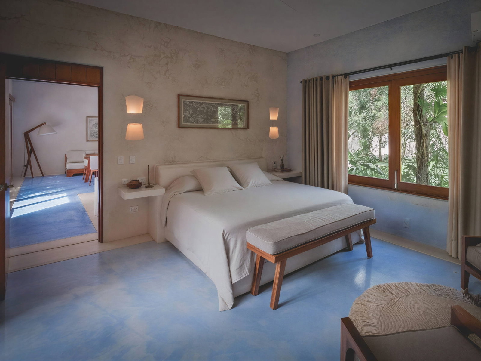 Casa de Arbol master bedroom at Wakax Hacienda with a white bed, beige walls, wooden bench, and a window showing greenery. Blue floor leads to a lit room with modern decor.