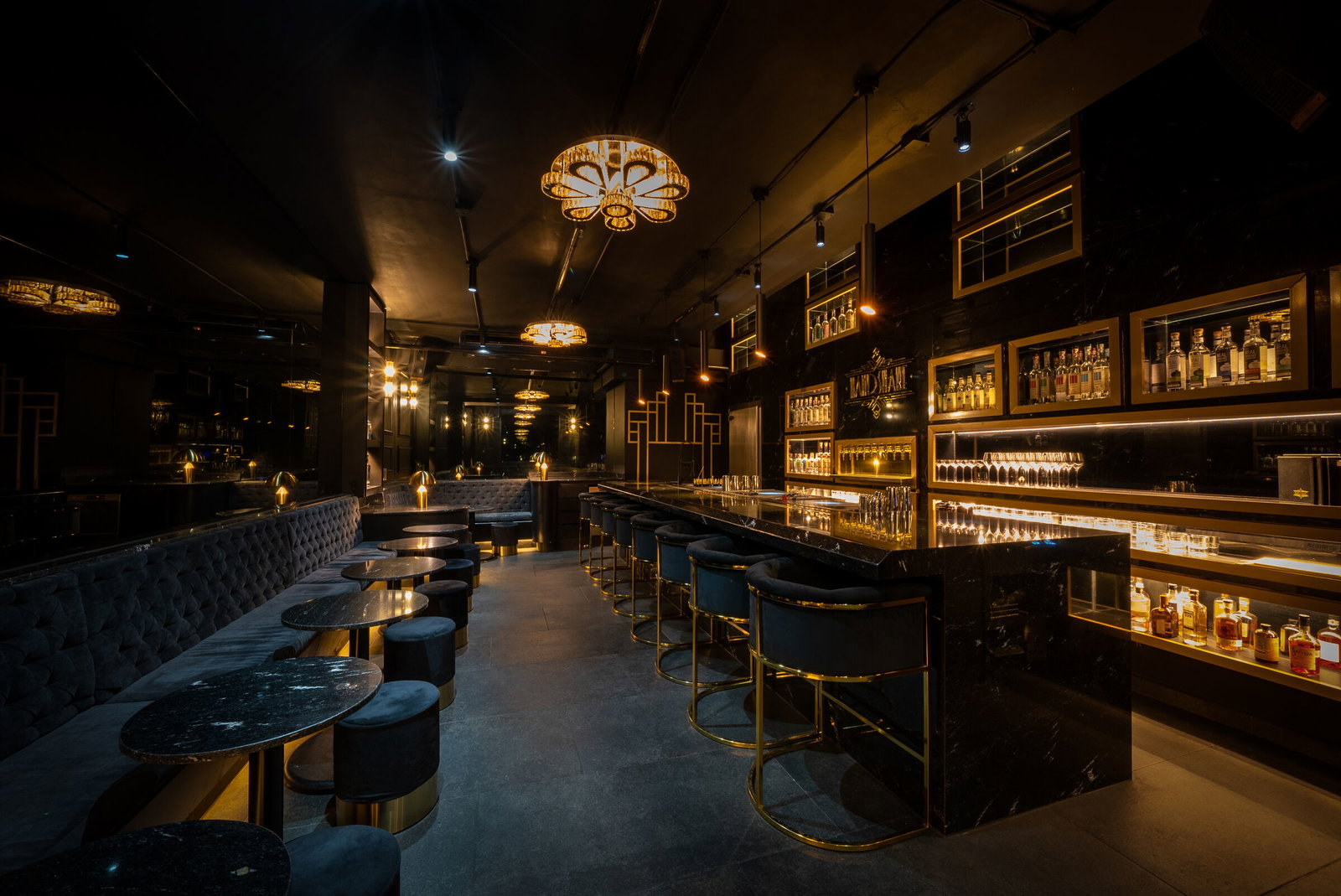 Luxurious bar interior with dark velvet seating, gold accents, and illuminated liquor shelves. Warm ambient lighting creates an elegant mood.