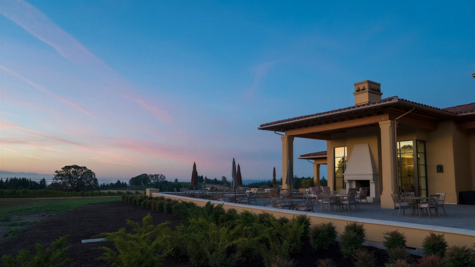Large building terrace at sunset, with empty chairs and closed umbrellas. Sky is pink and blue, creating a calm and serene atmosphere.