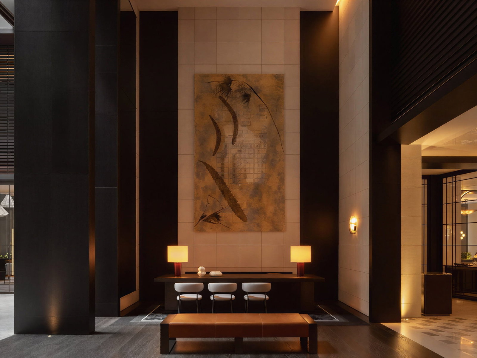 Capella Sydney Reception with abstract art, three chairs at a wooden table, warm lighting. Black pillars and greenery add contrast, creating elegance.