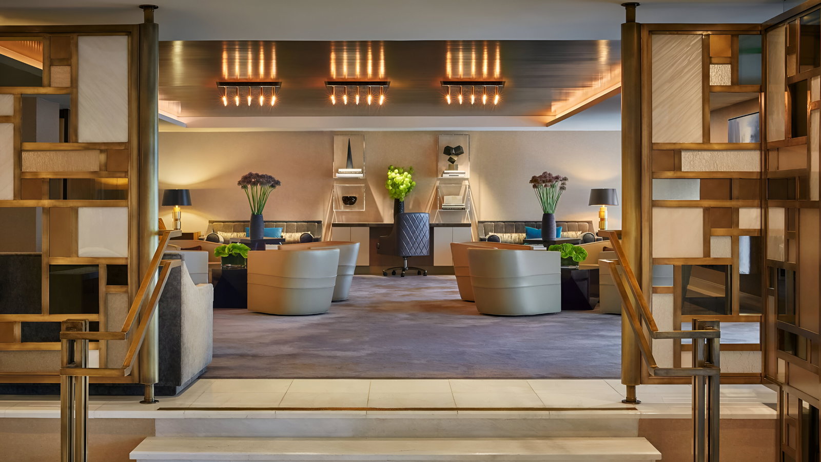 Luxurious lounge with beige chairs, geometric decor, and soft lighting. Vases of flowers add color to the elegant, modern interior.