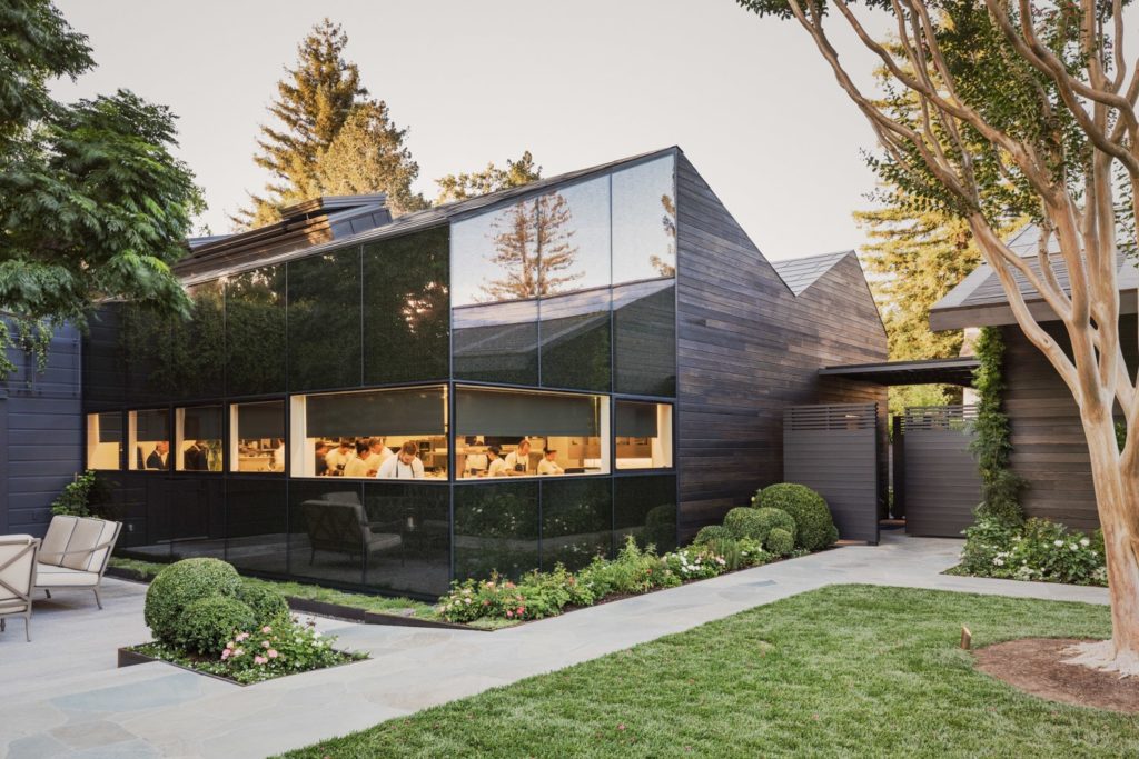 A sleek, modern black building with a window into the kitchen where chefs work busily.