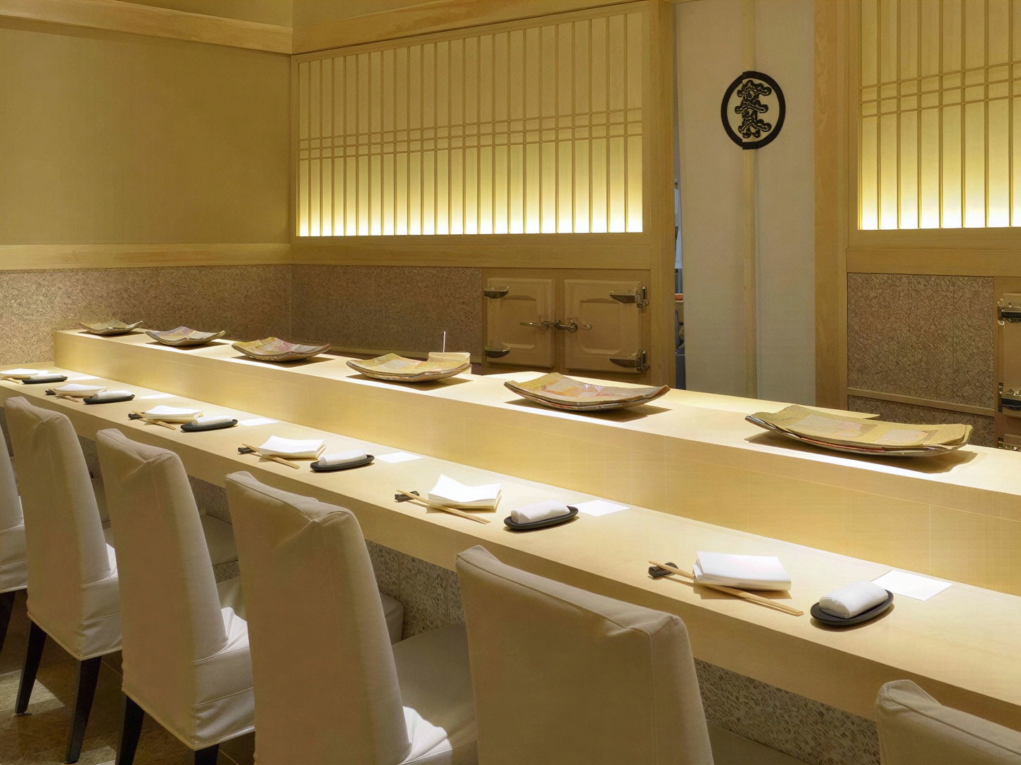 Elegant sushi bar with white chairs, neatly arranged chopsticks, and neutral tones. Subtle lighting creates a calm, inviting atmosphere.