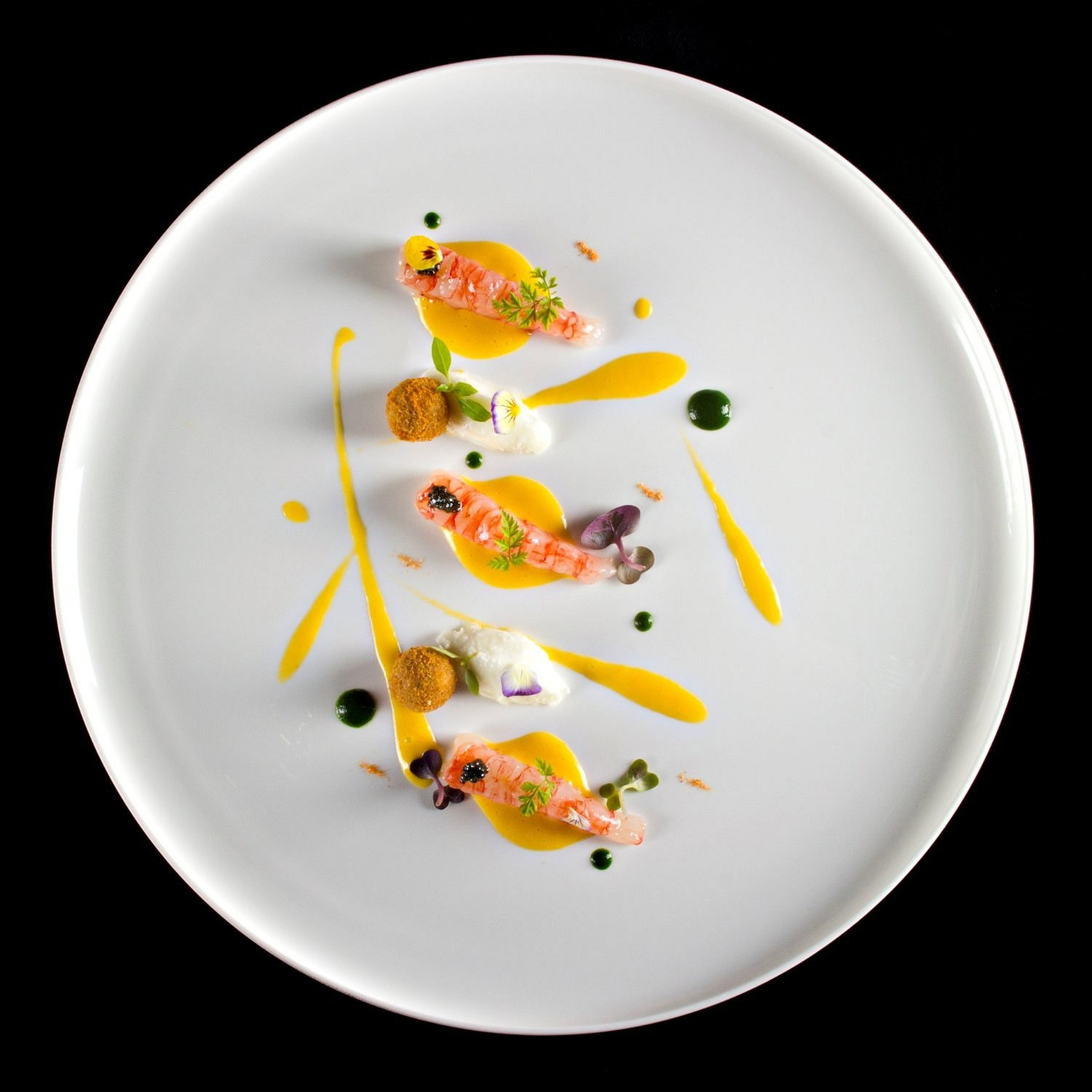 Elegant dish on a white plate with vibrant sauces, decorated with herbs and edible flowers, placed against a black background.