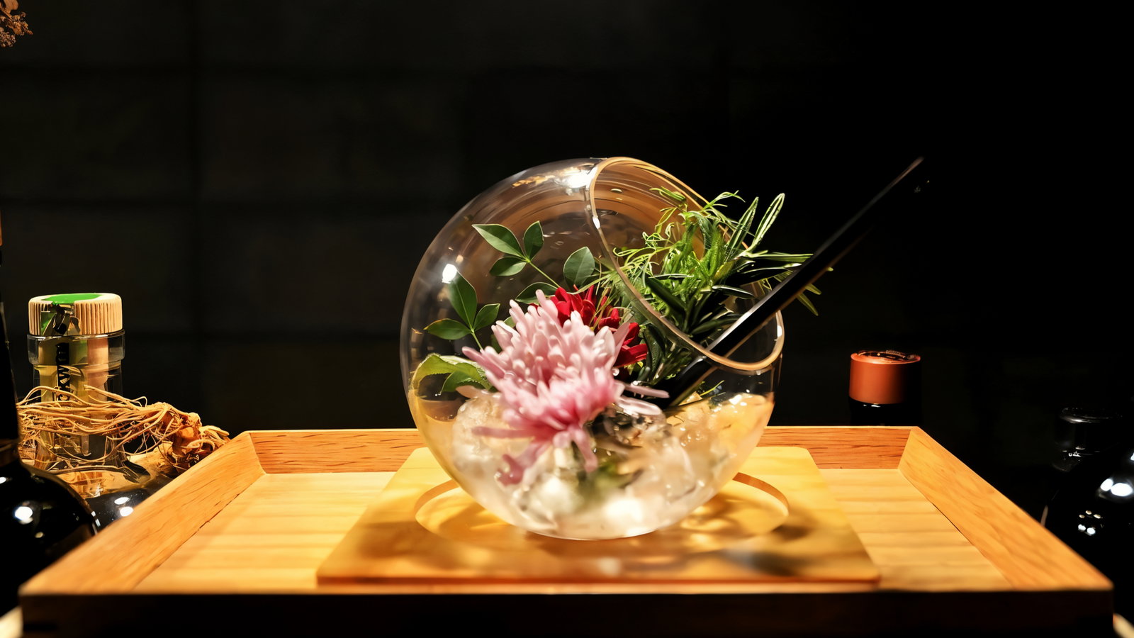 Ornamental glass bowl with pink and red flowers, green leaves, and straw on a wooden tray in a dimly lit setting.