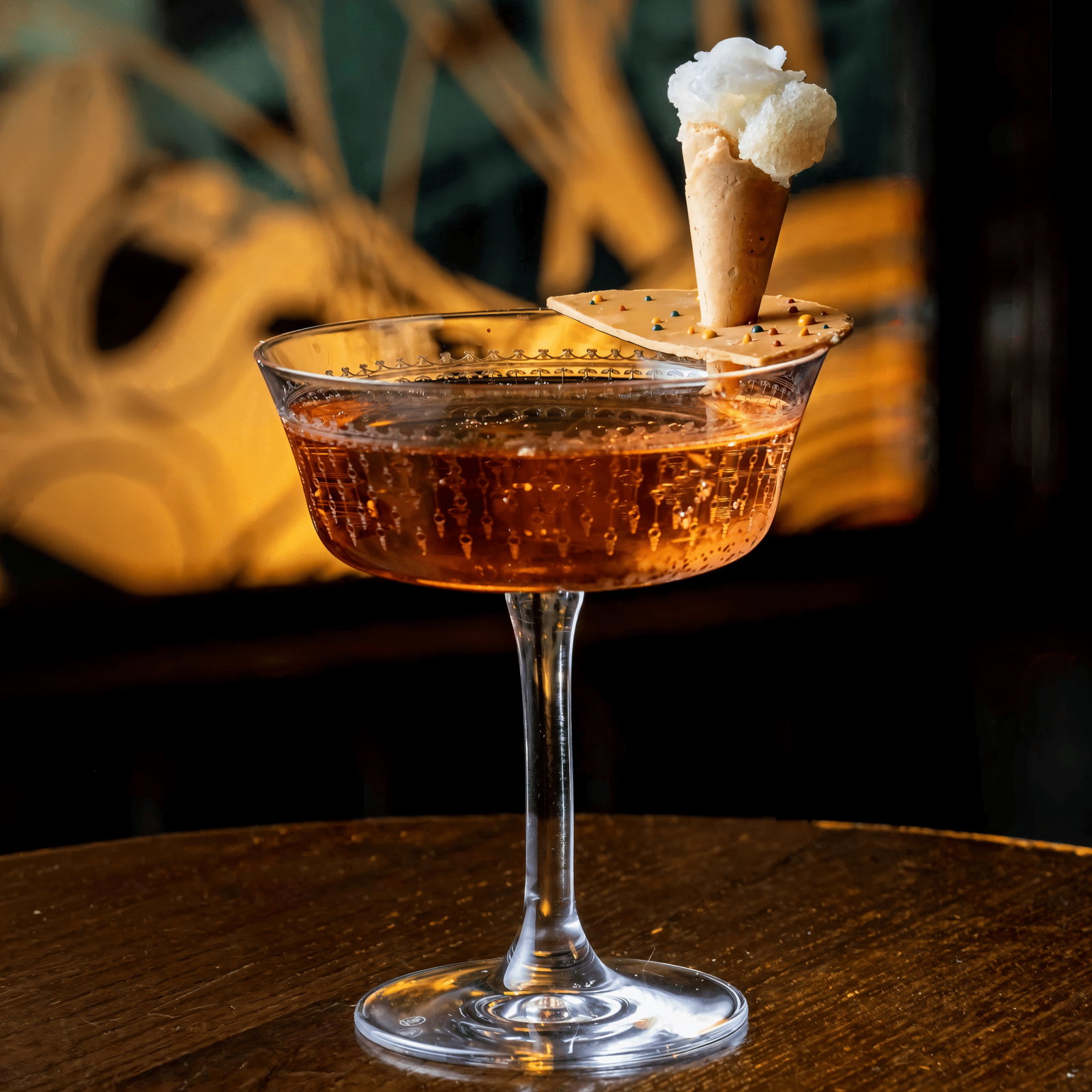 A sparkling cocktail in a glass with a mini cone on a cracker garnish. Warm, artistic background. Elegant and inviting mood.