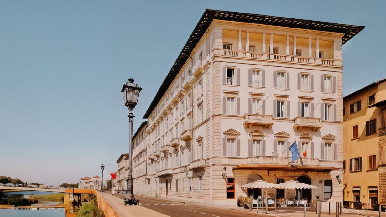 Historic building with white facade and balconies, located by a riverside. Flags at entrance, clear sky, and street lamps line the path.
