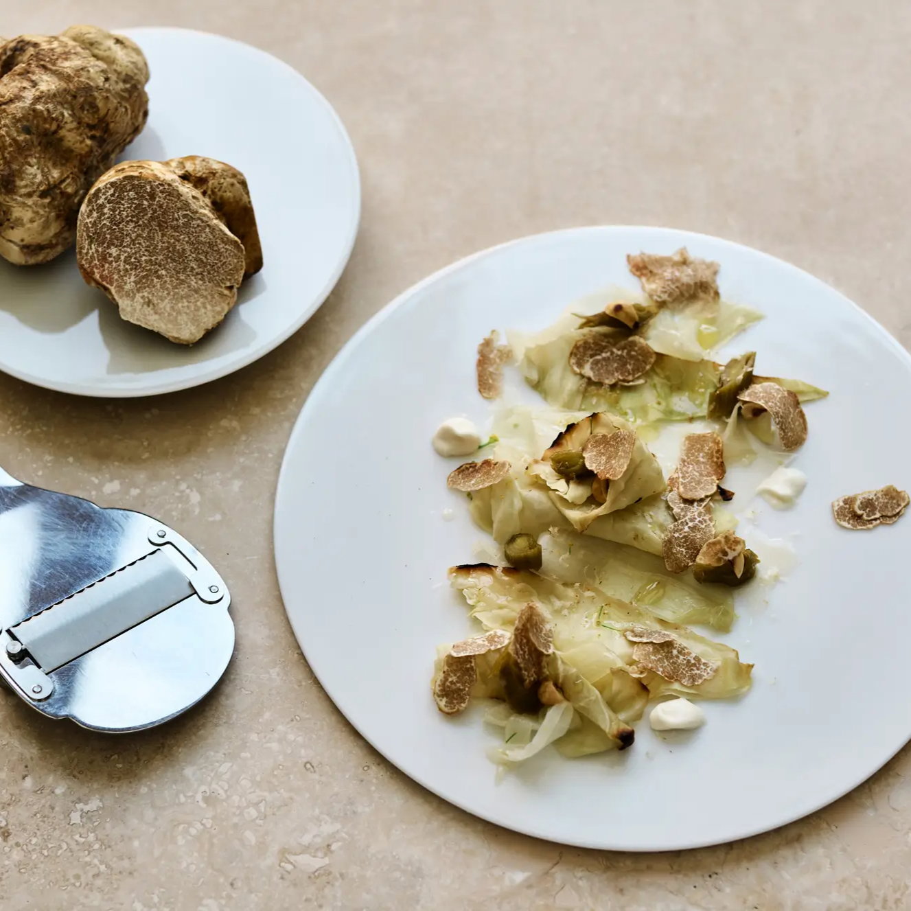 White truffle shavings on a plate with artichoke. Truffle slicer nearby. Beige background. Rustic and elegant presentation.