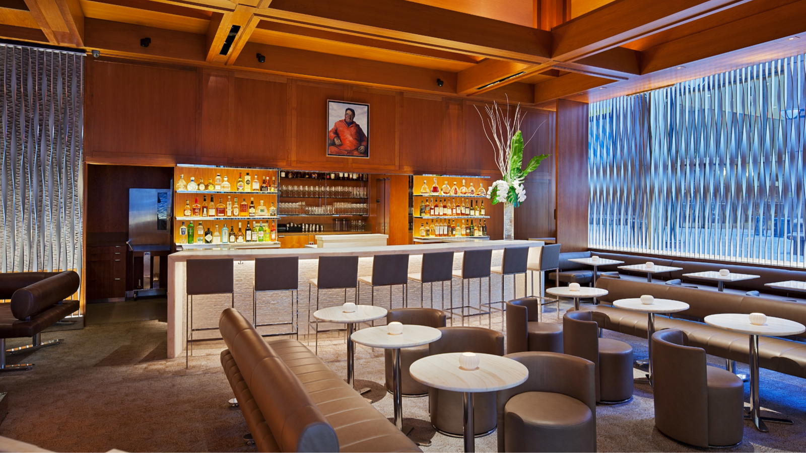 Elegant bar interior with leather seating, modern tables, and a well-stocked bar. Warm wood accents, abstract wall artwork, and floral decor.