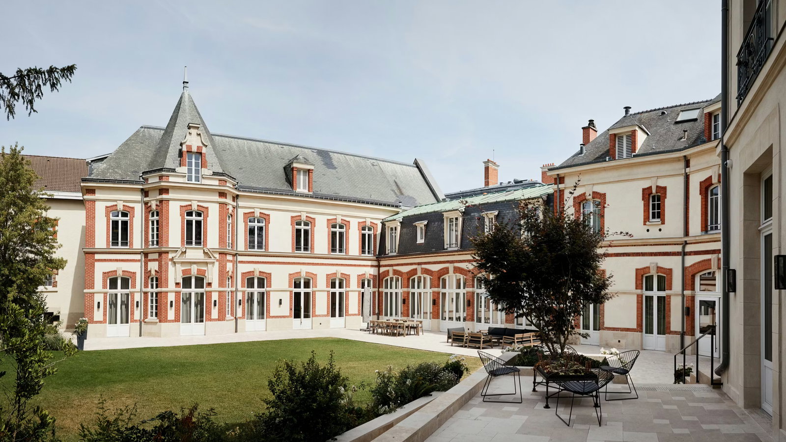 Historic mansion with red brick accents and slate roof in a serene courtyard. A lawn and patio furniture create a peaceful ambiance.