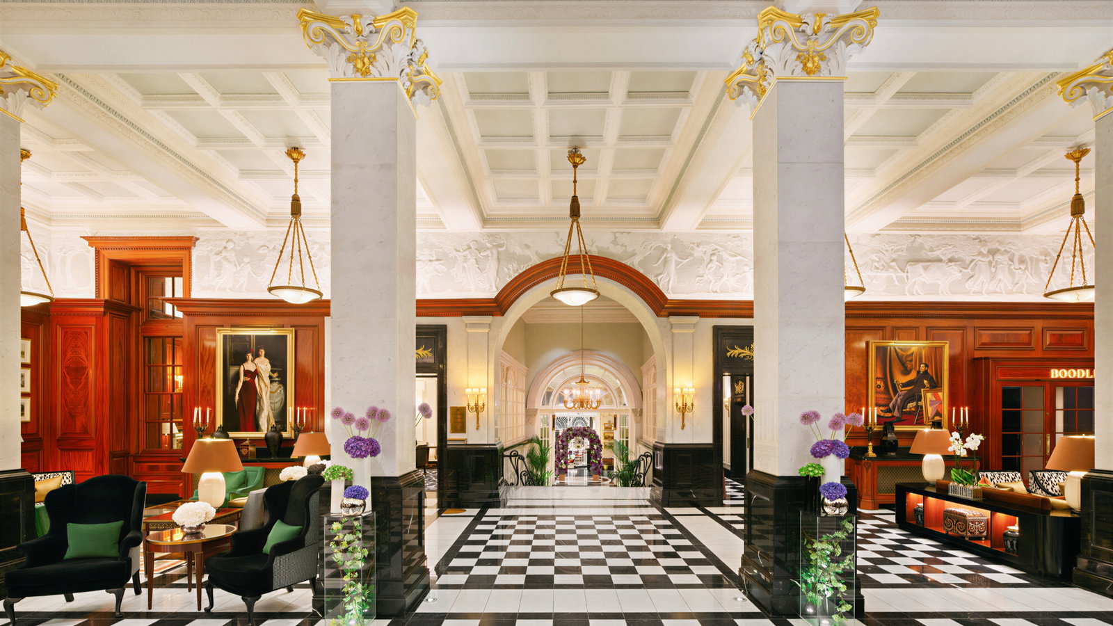 Elegant hotel lobby with marble columns, checkered floor, redwood accents, floral arrangements, chandeliers, and a painting. Regal ambiance.