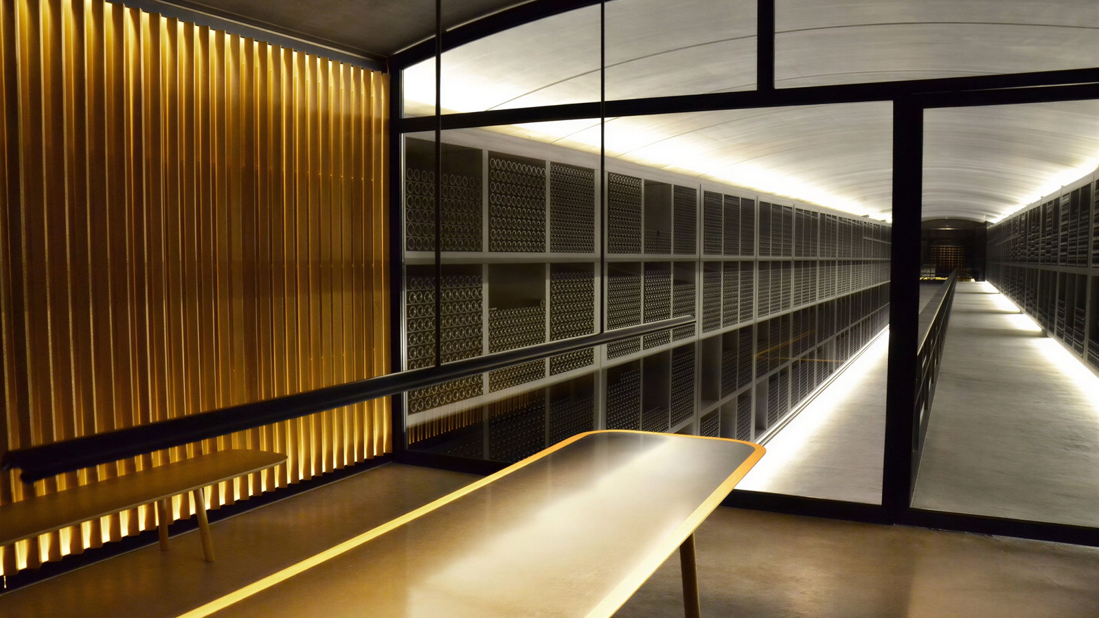 Dimly lit wine cellar with rows of wine bottles on shelves. A long corridor with reflective surfaces and warm yellow lighting creates a serene mood.