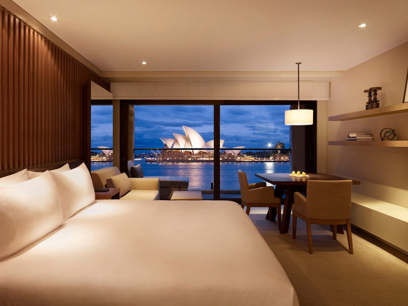 Opera Room at Park Hyatt Sydney a plush bed, dining area, and a view of the Sydney Opera House through large windows at dusk, creating a cozy vibe.