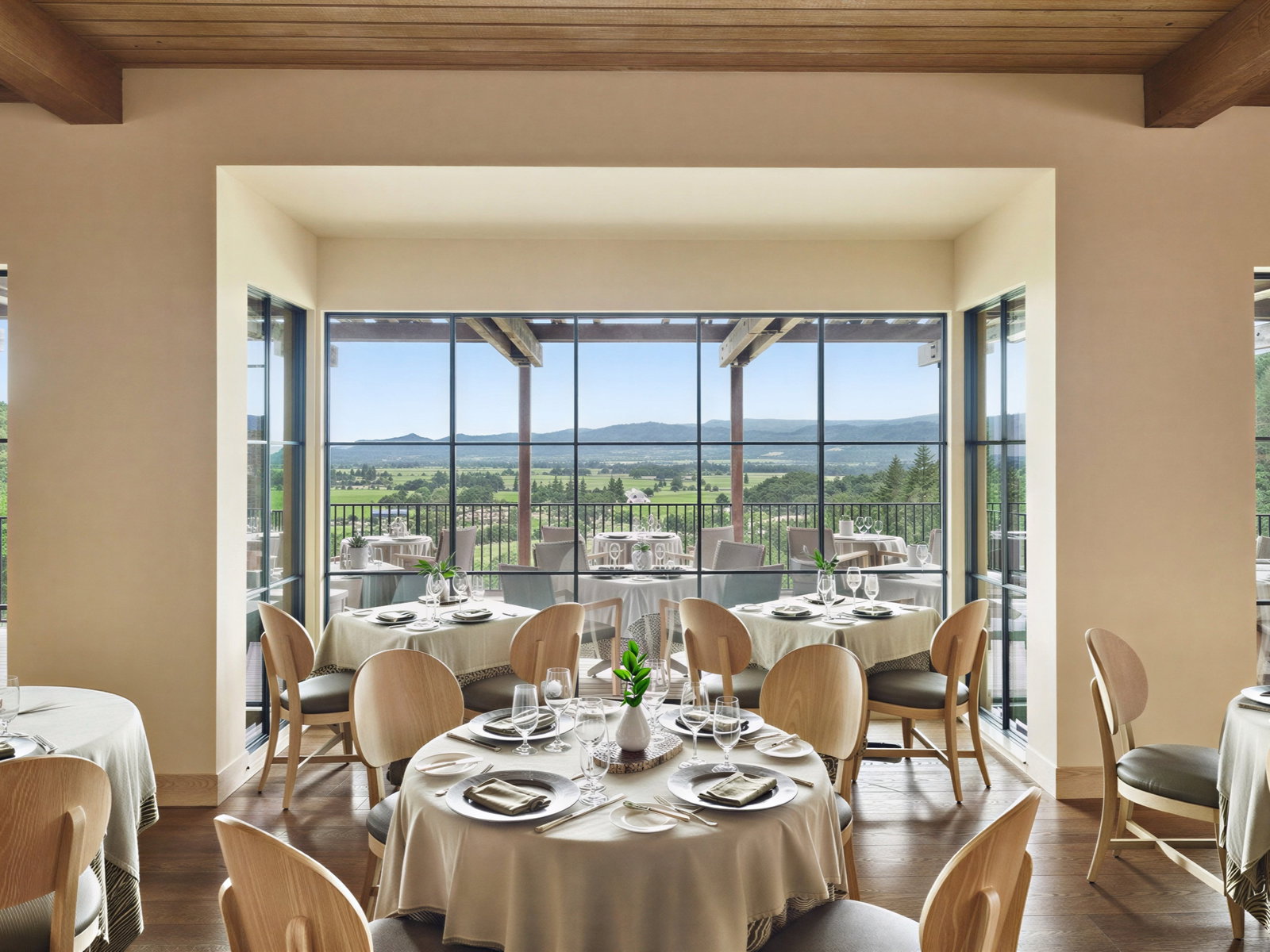 Elegant dining room with set tables, neutral tones, large windows showcasing scenic view of green fields and mountains, creating a serene ambiance.