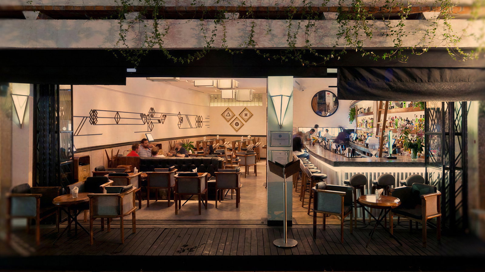 Cozy café with geometric wall art and warm lighting. Patrons seated at tables and bar. Plants decorate the scene. Relaxed ambiance.