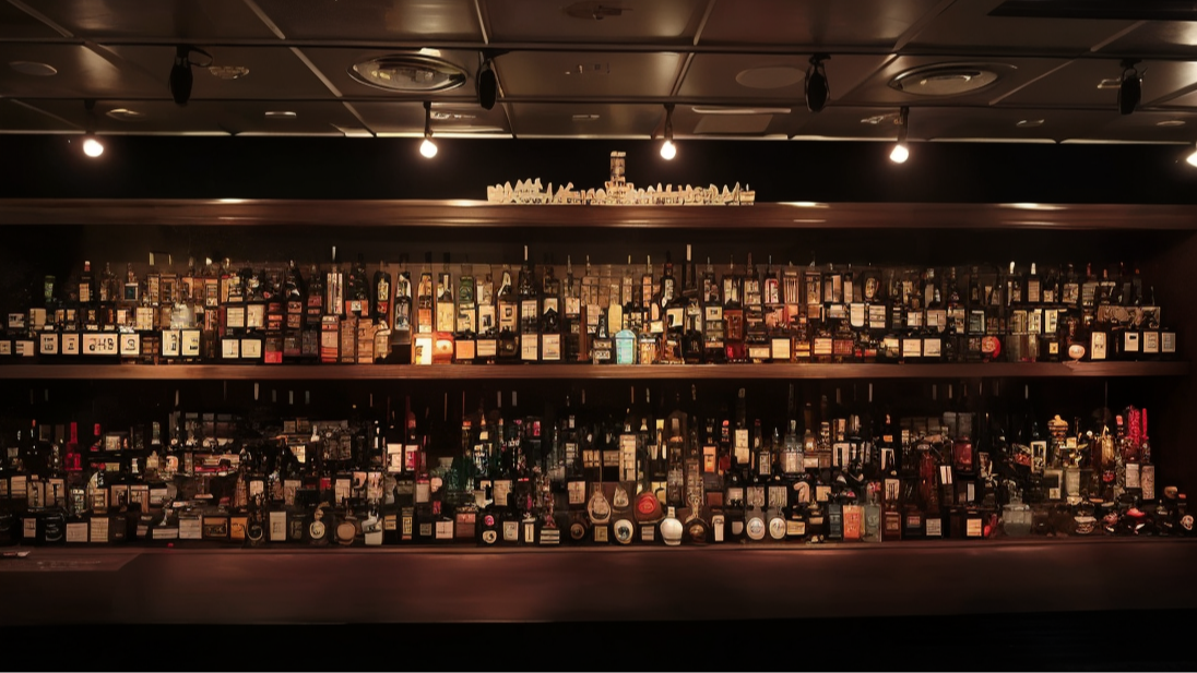 Bar shelves filled with an array of liquor bottles in diverse shapes and colors, dimly lit from above. Warm, inviting atmosphere.