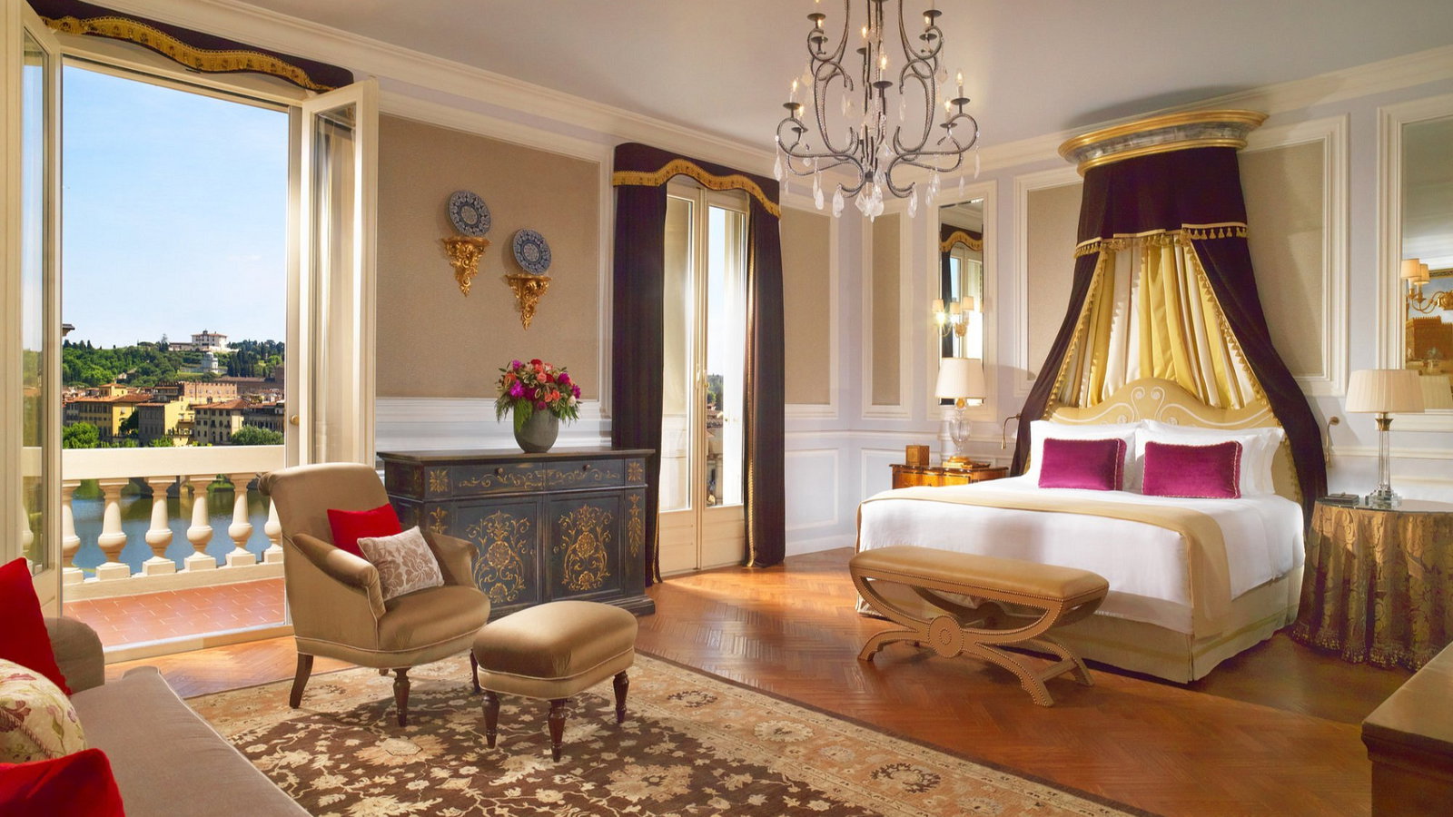 Luxurious bedroom with a canopy bed, elegant chandelier, and ornate furnishings. Open doors reveal a scenic city view. Warm, opulent vibe.