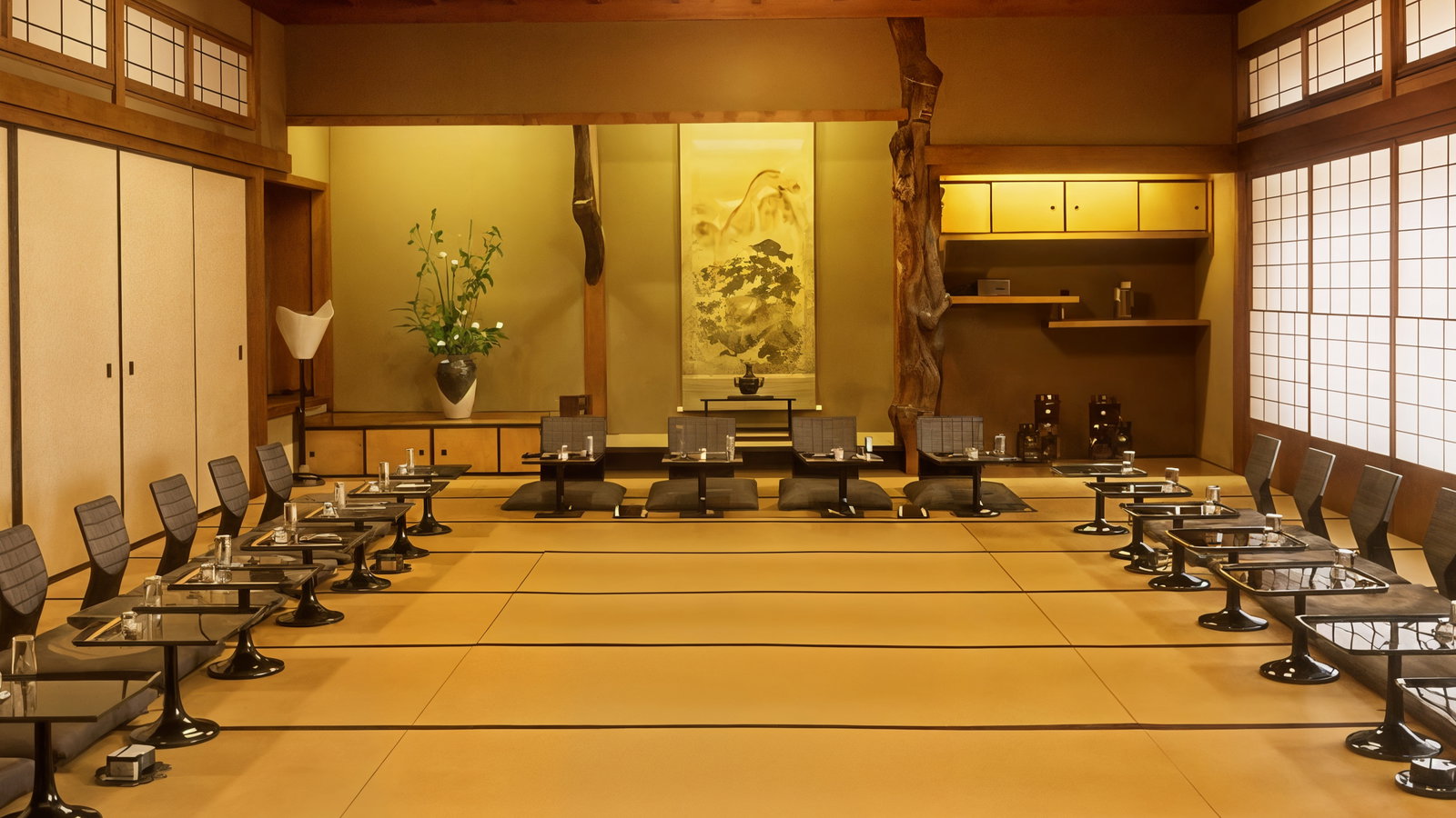 Traditional Japanese tatami room with low black tables and chairs arranged symmetrically. Soft lighting, floral arrangement, and shoji screens.