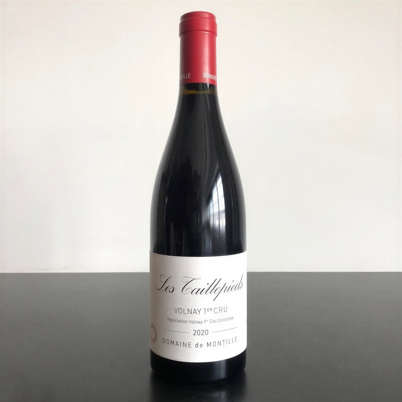 Red wine bottle labeled "Les Taillepieds, Volnay 1er Cru, 2020" on a black surface with a plain white background.