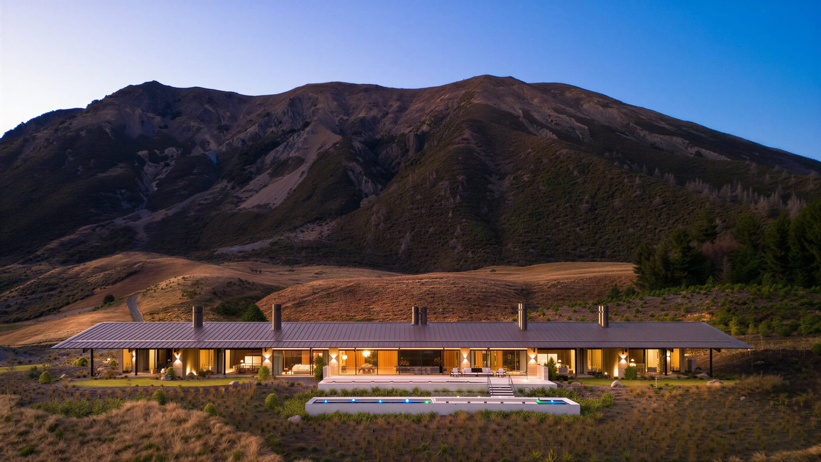 Flockhill Lodge exterior with a pool is set against a mountainous backdrop at dusk. The landscape is dry with warm lighting, creating a serene mood.