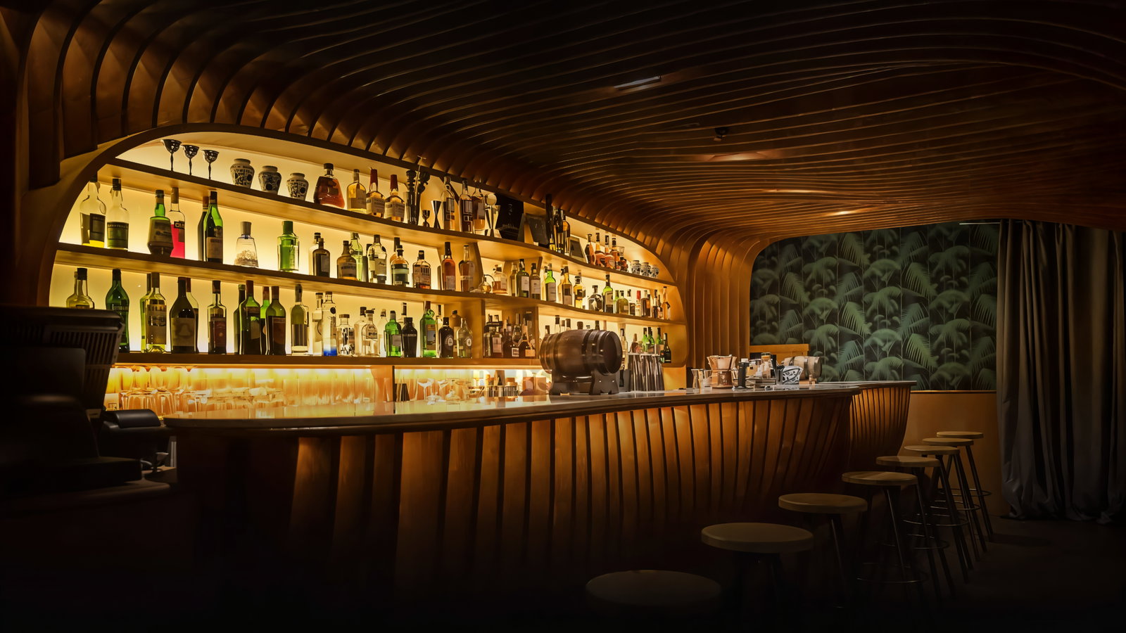 Cozy bar with wooden decor, shelves of colorful bottles, and a patterned green backdrop. Empty bar stools line the counter.