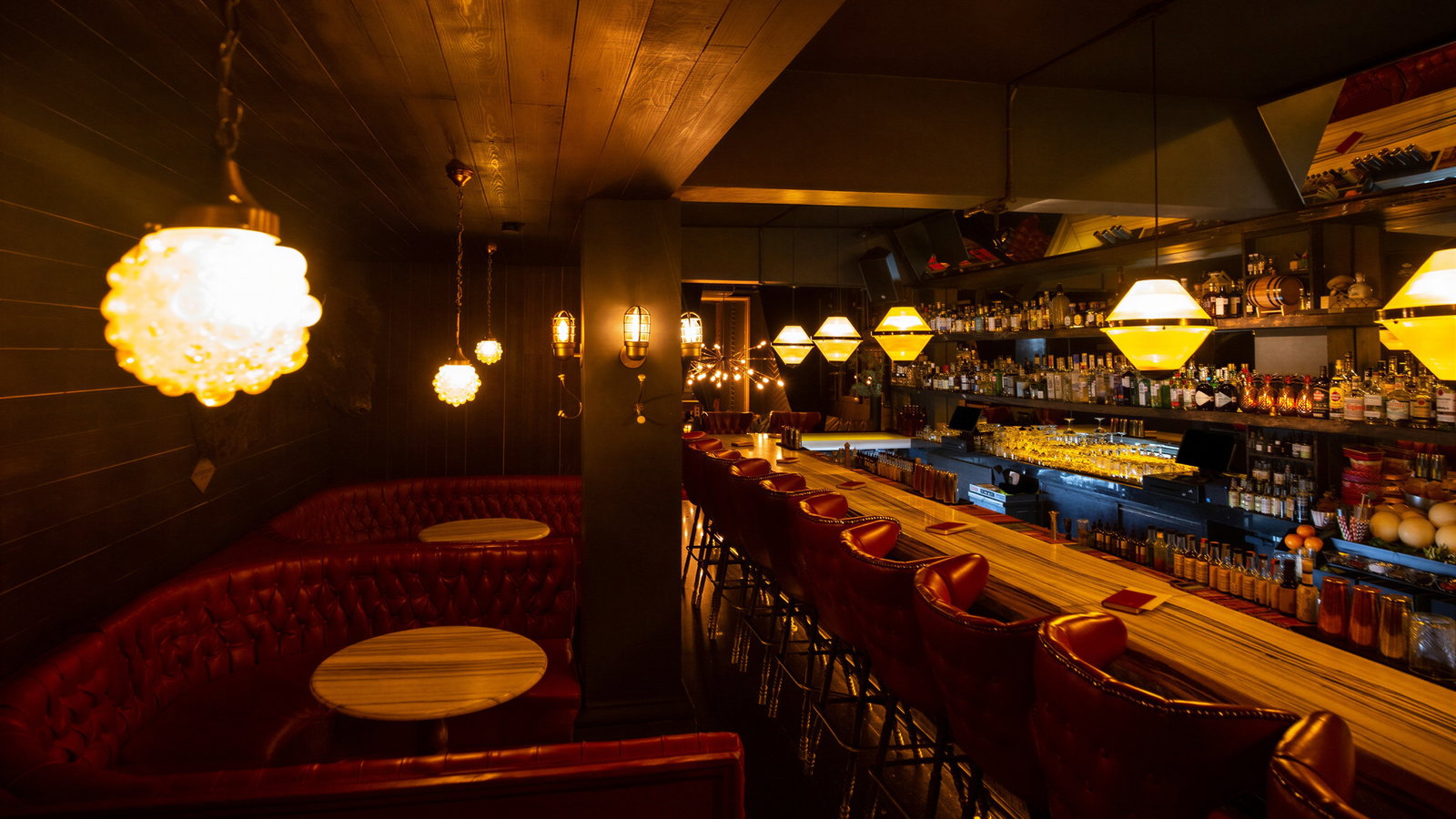 Cozy bar with a wooden interior, red leather booths, glowing lamps, and a stocked bar. Warm ambiance, inviting for relaxation.