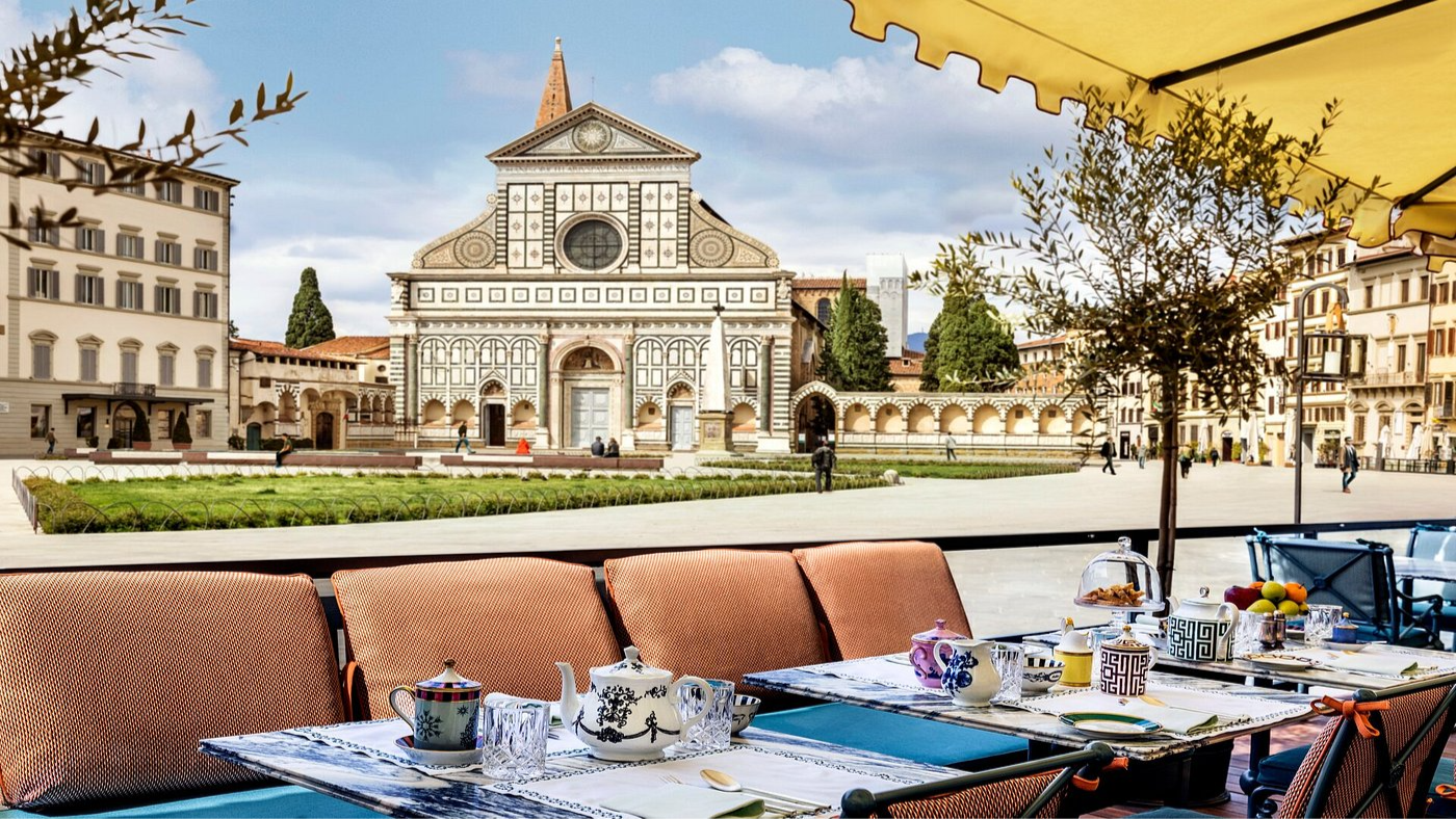 Outdoor cafe with colorful teapots and cups on a table under a yellow canopy, facing a historic cathedral with ornate facade under a blue sky.