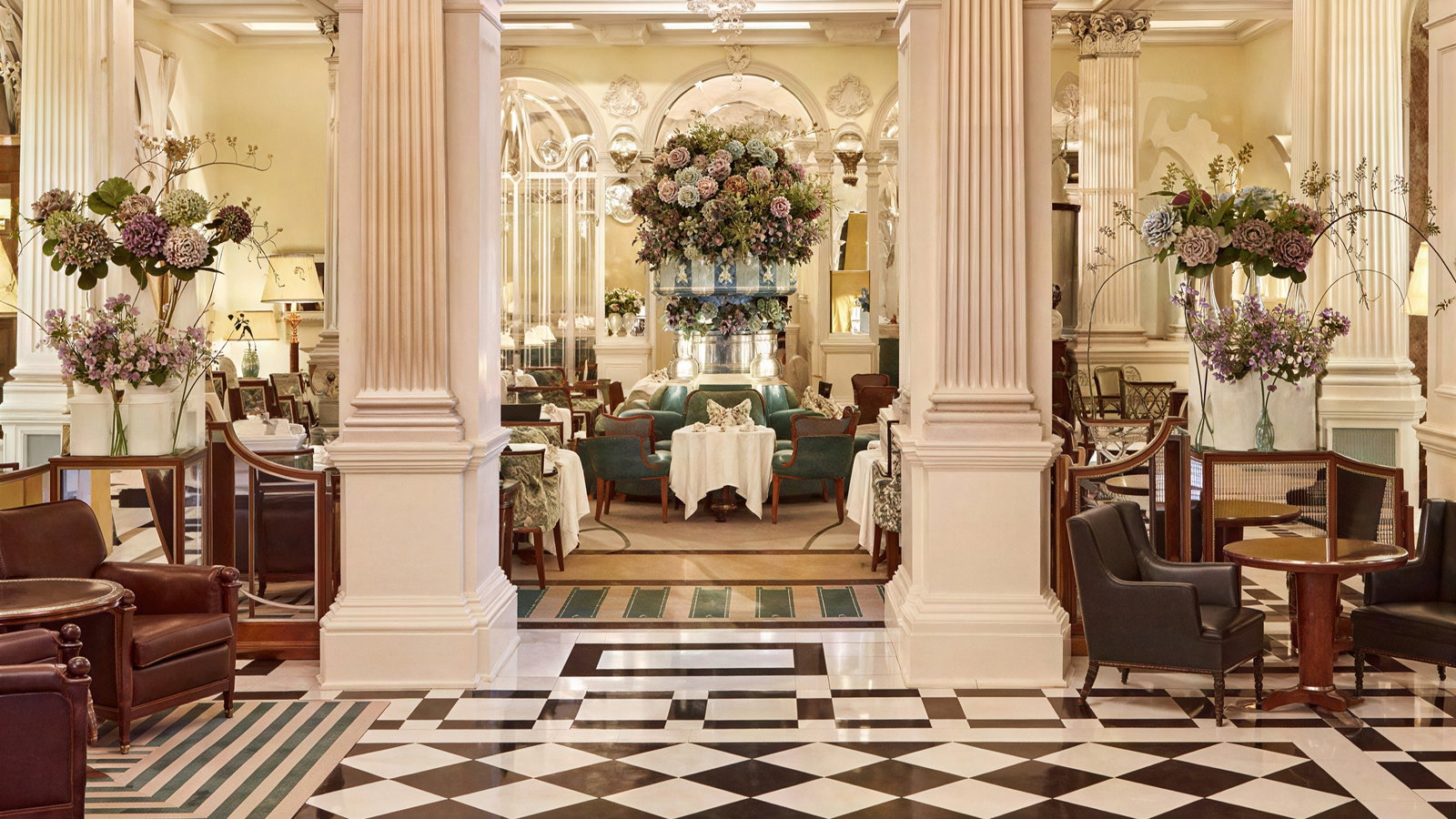 Luxurious cafe interior with elegant columns, floral arrangements, and plush seating. Black-and-white checkered floor enhances opulence.