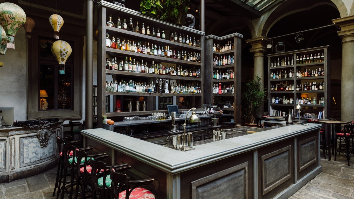 Elegant bar with wooden shelves stocked with liquor bottles, surrounded by vintage decor and hot air balloon lampshades. Cozy ambiance.