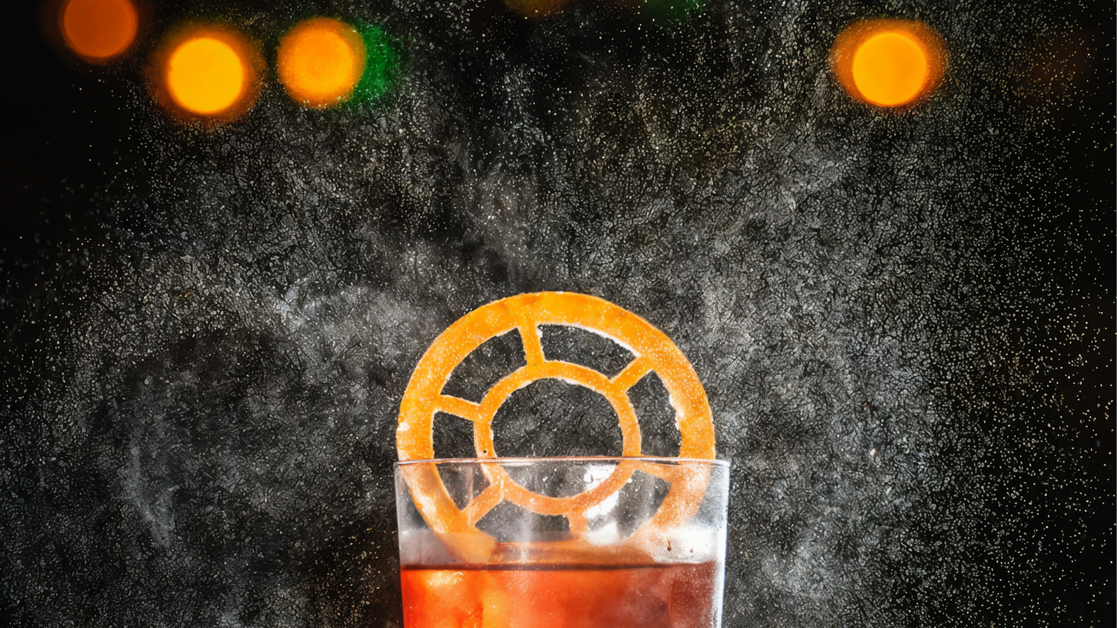 A glass with an orange slice and a red drink, set against a dark background with glowing bokeh lights and a smoky effect, creating a moody vibe.