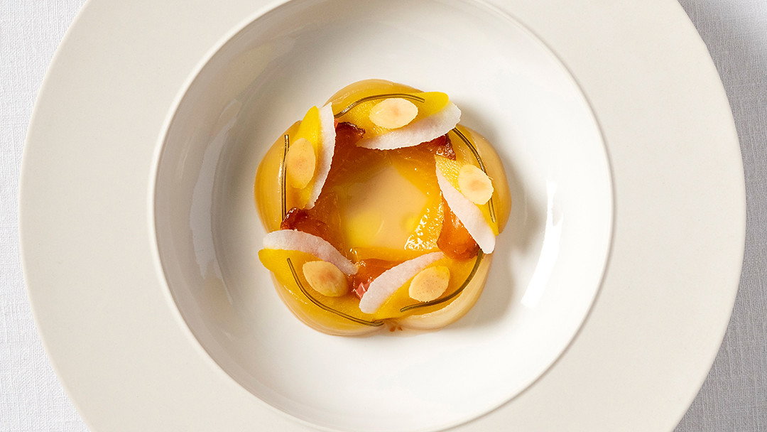 Elegant dessert on white plate, featuring sliced fruit and almond slivers arranged in a circle. Set on a textured white tablecloth.