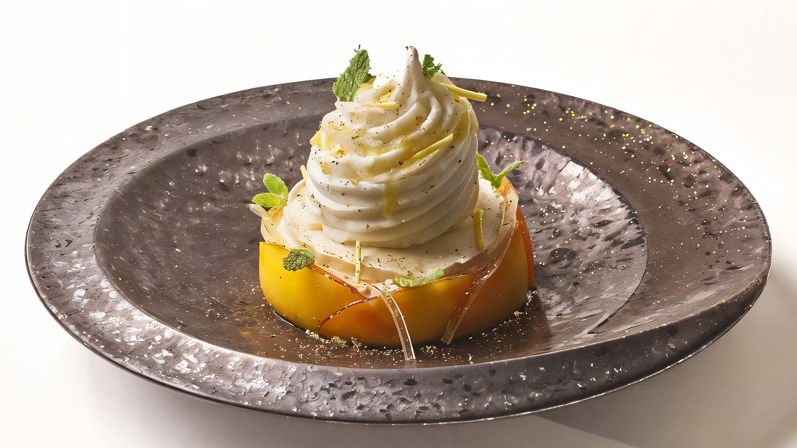 A dessert with swirled cream and garnishes on a sliced fruit base, served on a textured dark plate against a plain white background.