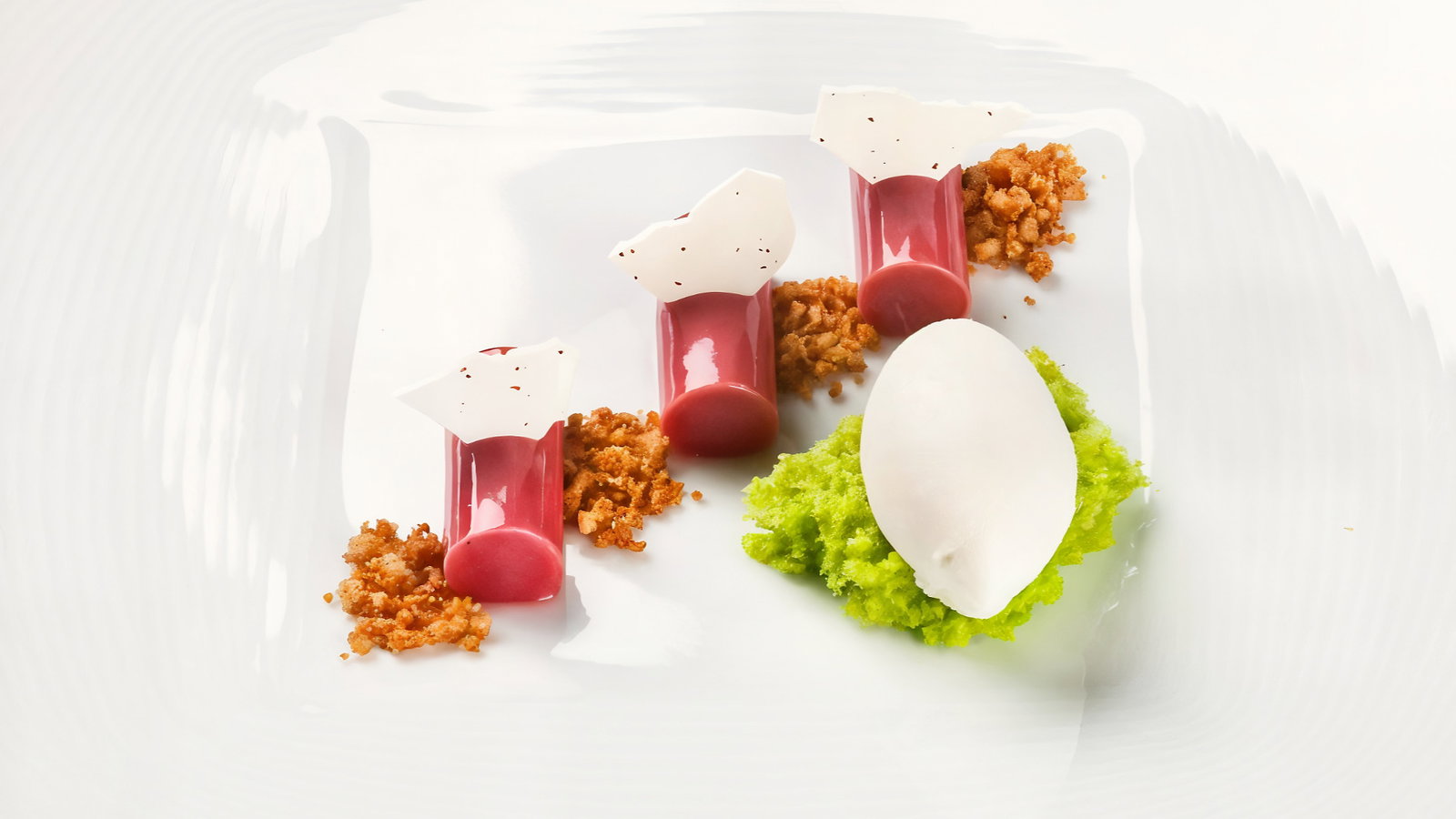 Gourmet dessert on a white plate: red cylinders, white shards, green puree, and white ice cream, creating an artistic presentation.