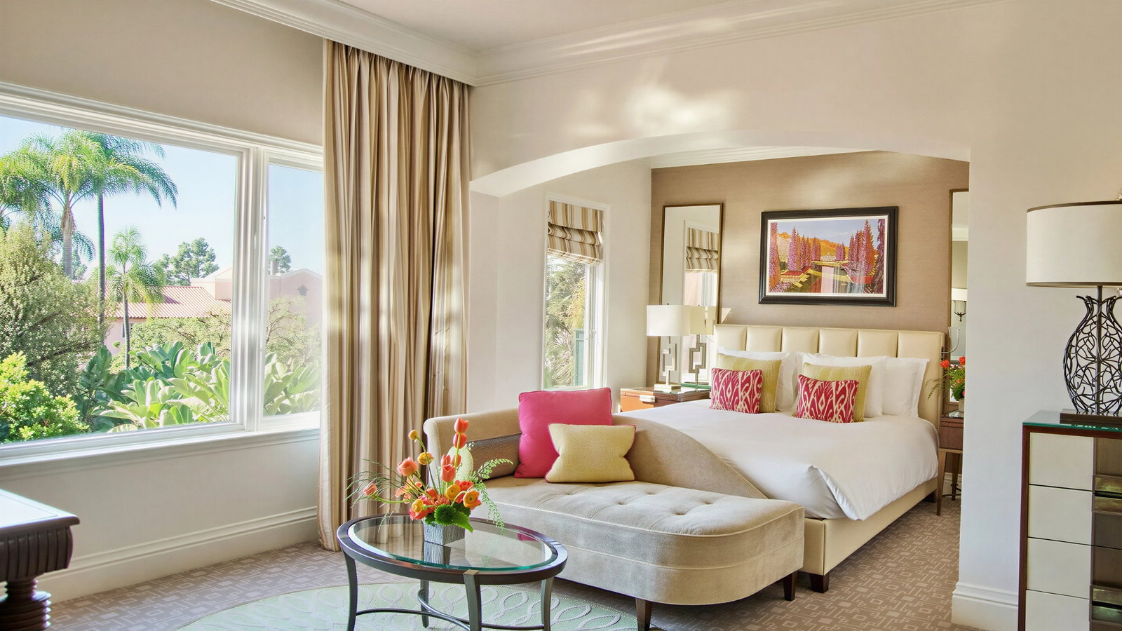 Bright bedroom with large window, lush view, a cozy bed adorned with pink pillows, a patterned rug, and a glass table with flowers. Calm mood.