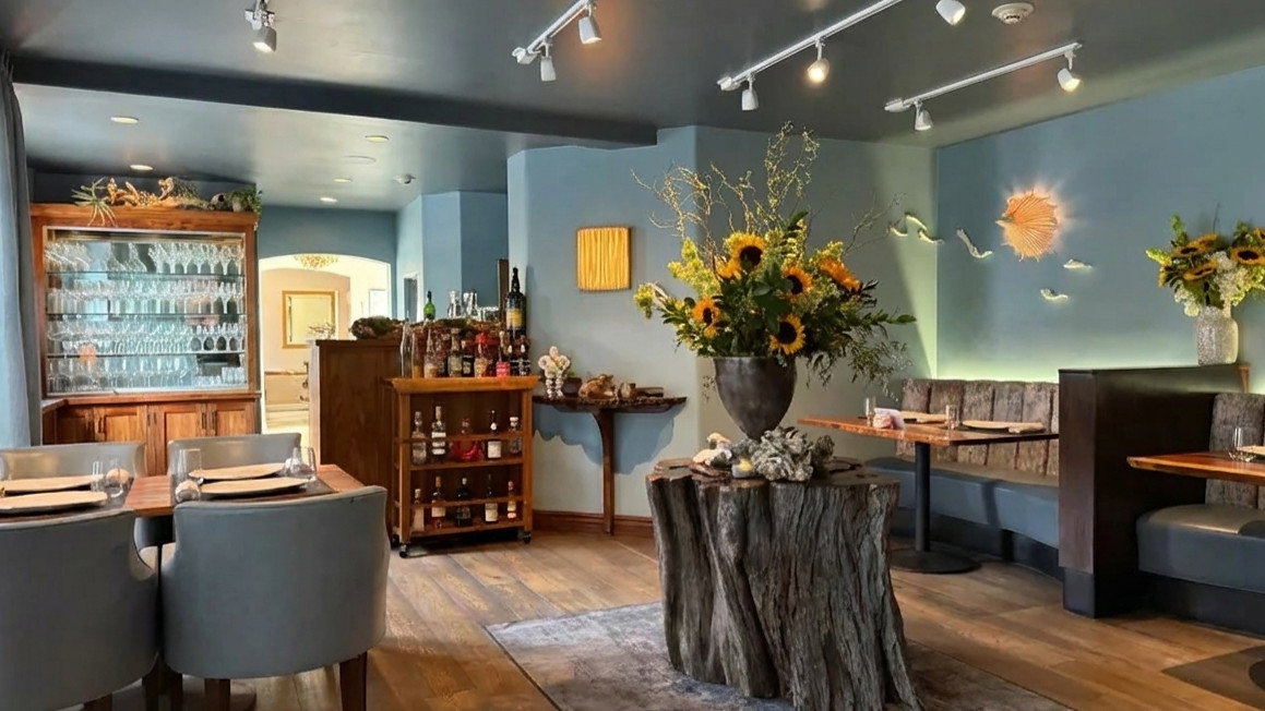 Cozy restaurant with wooden decor, blue walls, and a large sunflower bouquet on a tree stump table. Warm ambiance with elegant dining setup.