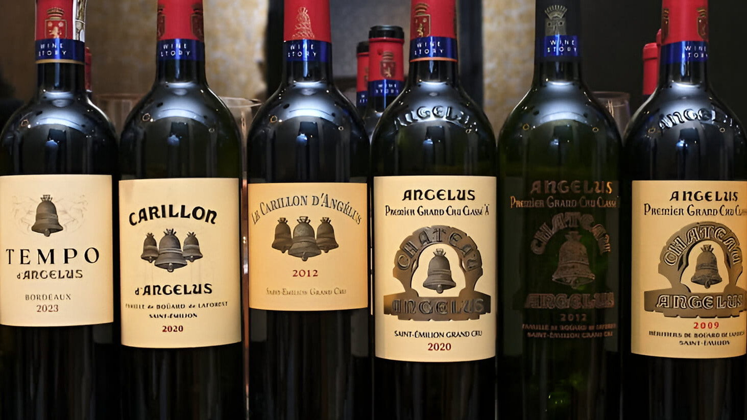 A row of Château Angélus wine bottles for their tasting with labels reading "Blanc du Milieu," "Tempo," "Carillon," and "Angélus" displayed on a shelf in a warmly lit room.