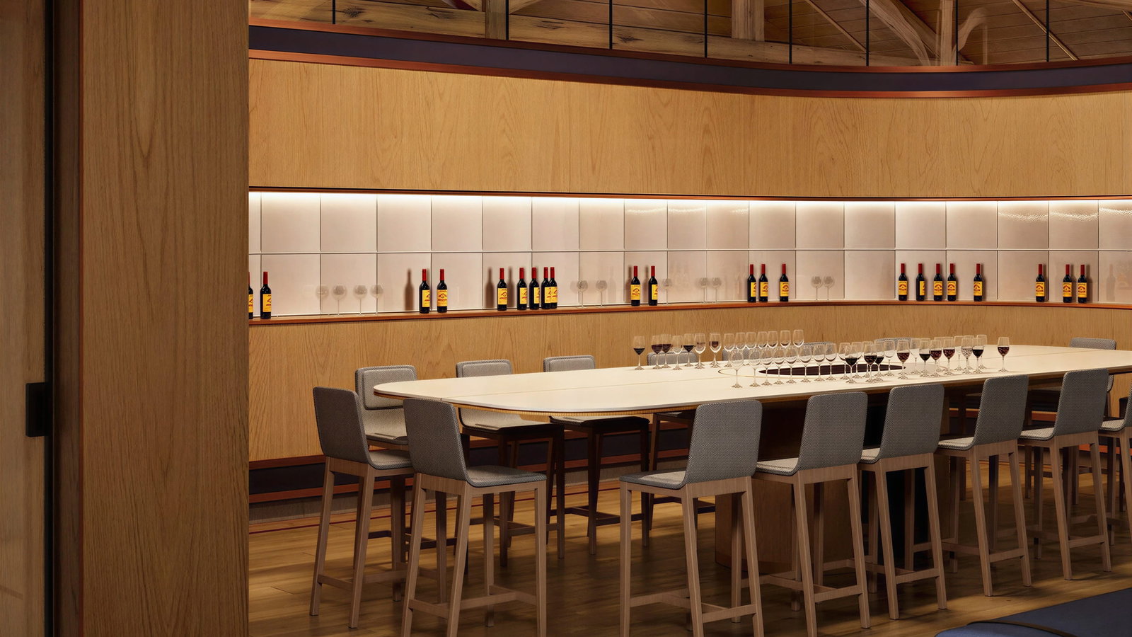 Wooden wine tasting room at Château Angélus with a long table, surrounded by gray chairs. Bottles and glasses are lined up in a well-lit, cozy setting.