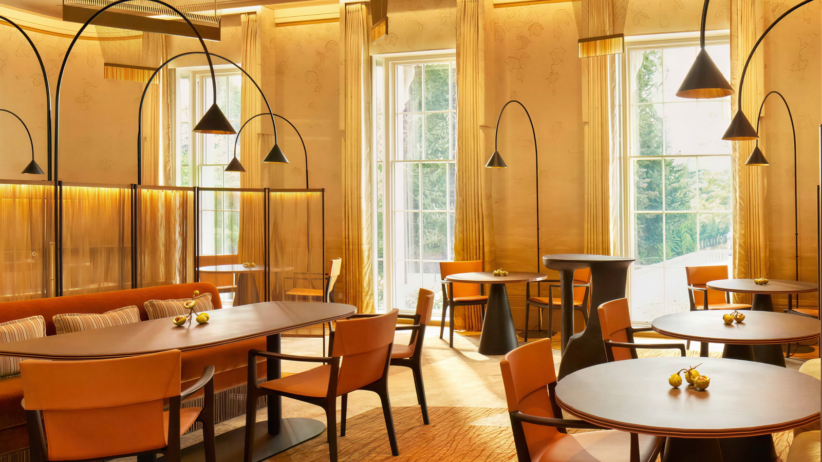 Elegant restaurant interior with orange chairs and wooden tables. Soft lighting, large windows, and warm tones create a cozy ambiance.