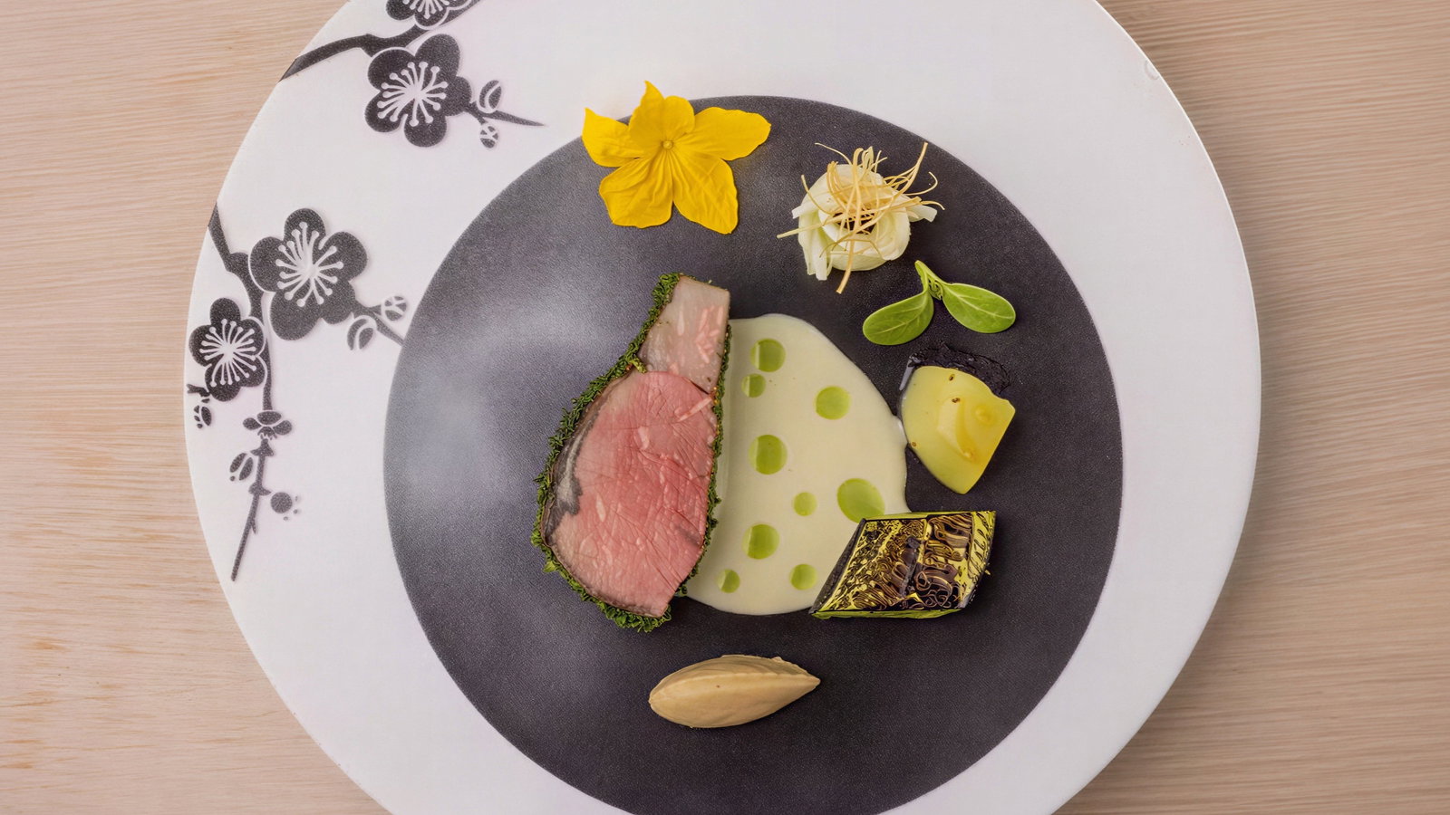 Elegant gourmet dish with sliced meat, sauce, flower garnish on a floral-patterned plate, set on a light wood surface.