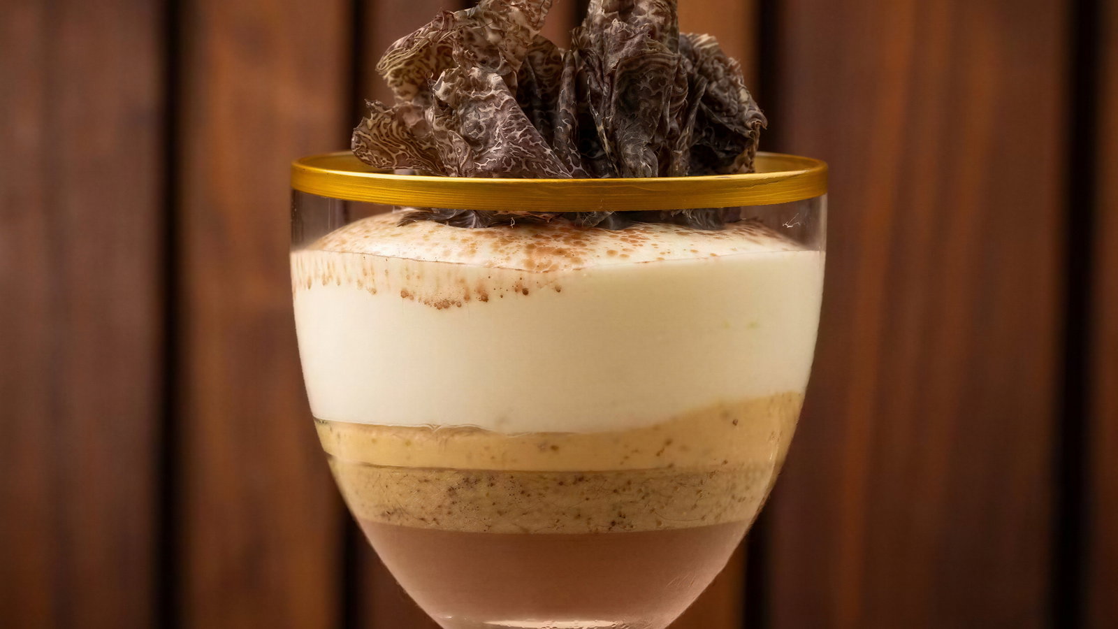 Layered dessert in a glass with chocolate, cream, and mousse topped with truffle shavings. Wooden background. Elegant presentation.